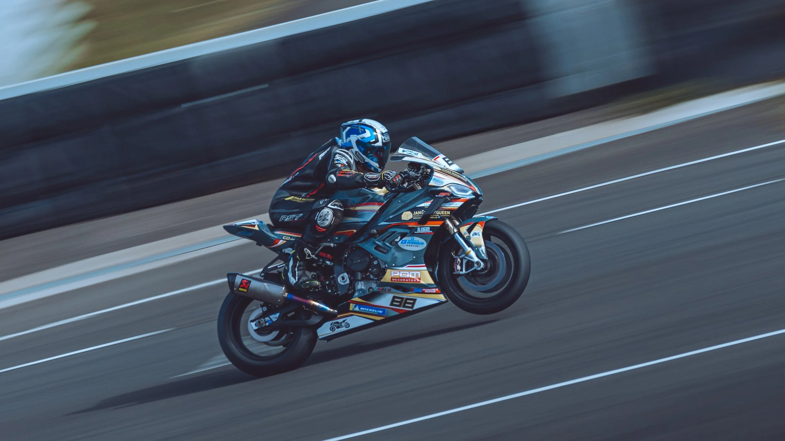 A motorcycle racer in a black racing suit and helmet riding a sport motorcycle on a race track during daytime.