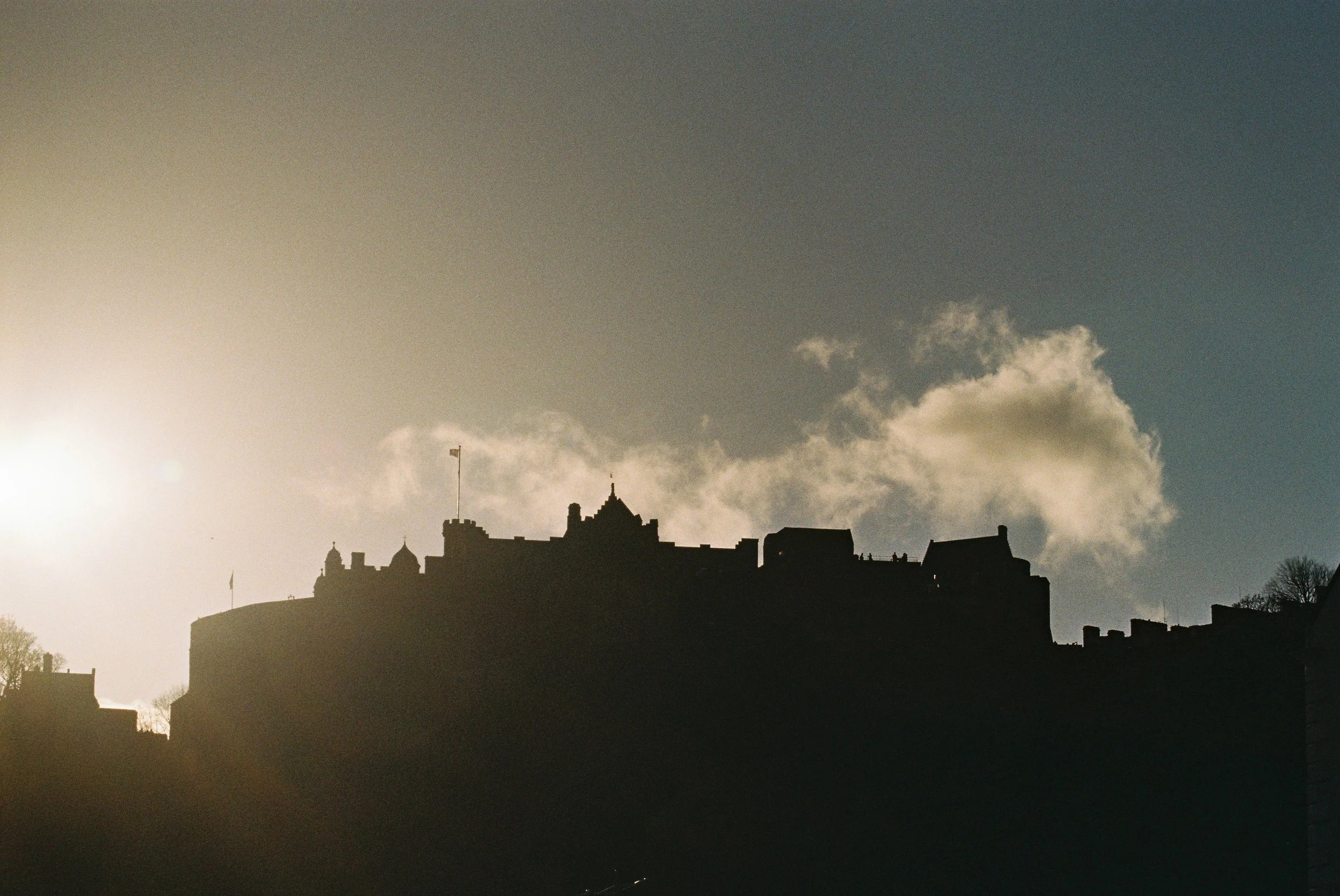 Silhouetted castle and buildings on a hill against a partly cloudy sky at sunset.