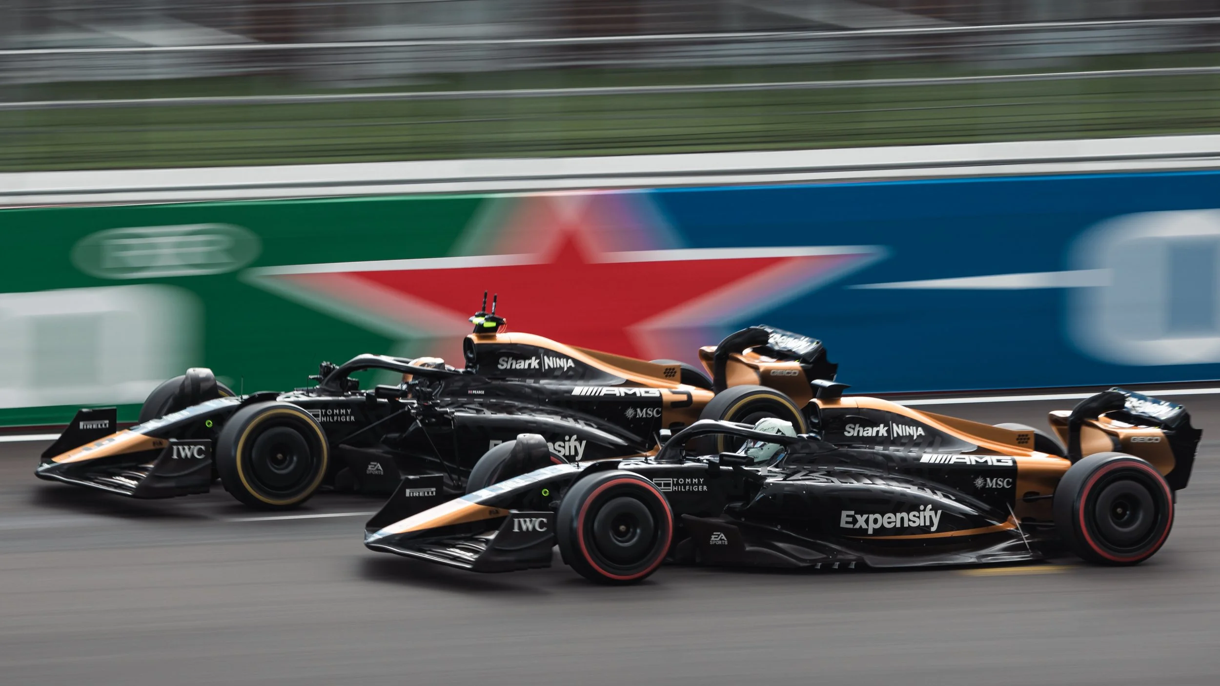 Race cars on track with sponsorship logos, including 'Expensify' and 'Shark Ninja', during a motorsport event.