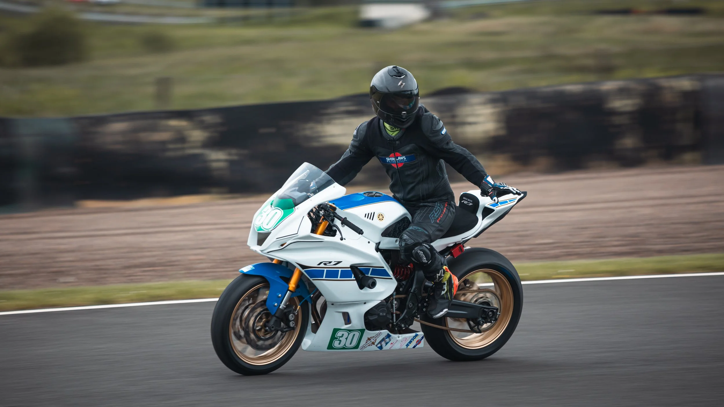 Motorcycle rider wearing black helmet and gear, riding a race bike on a track with blurred background.