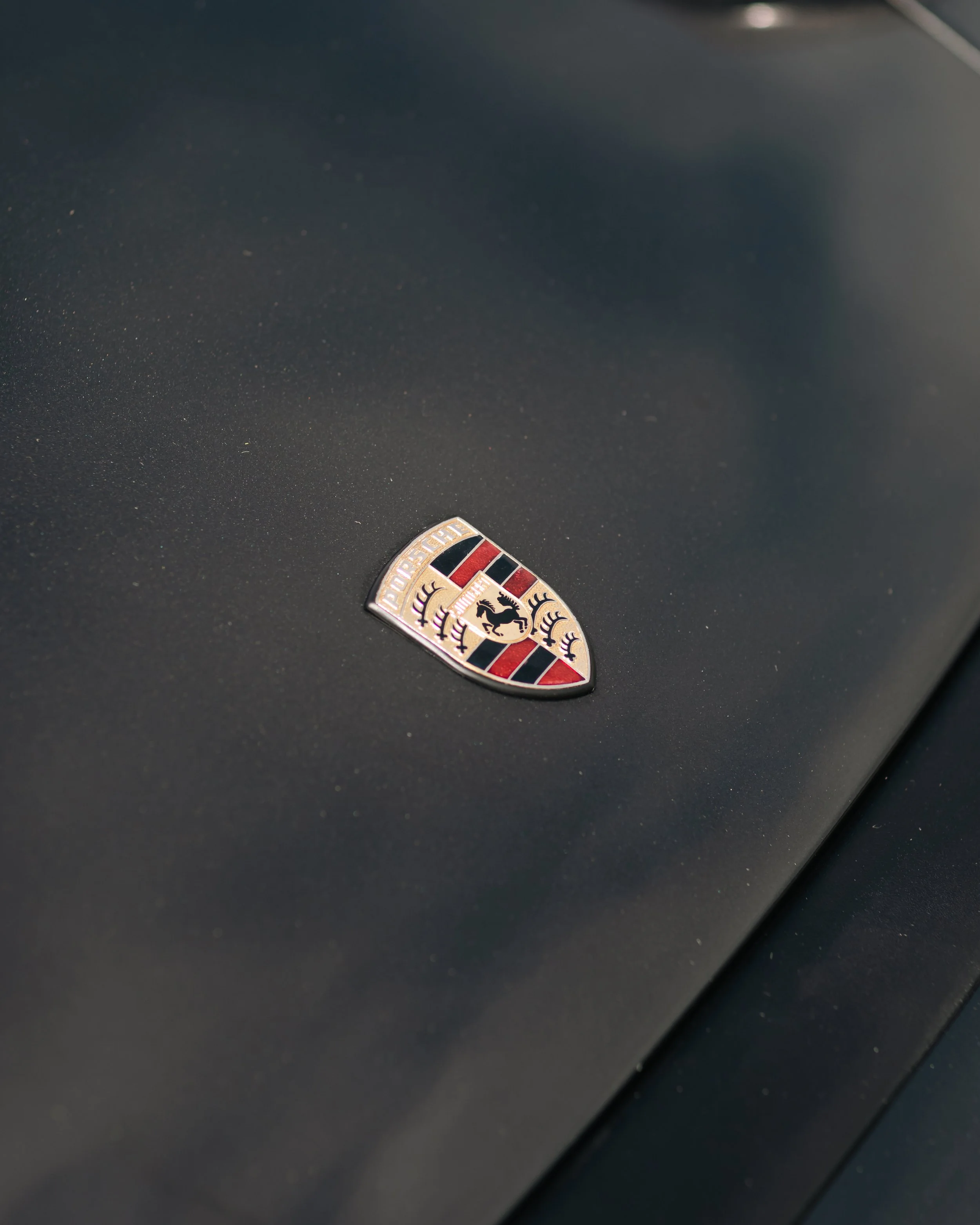 Close-up of a Porsche emblem on a car with a dark, textured surface.