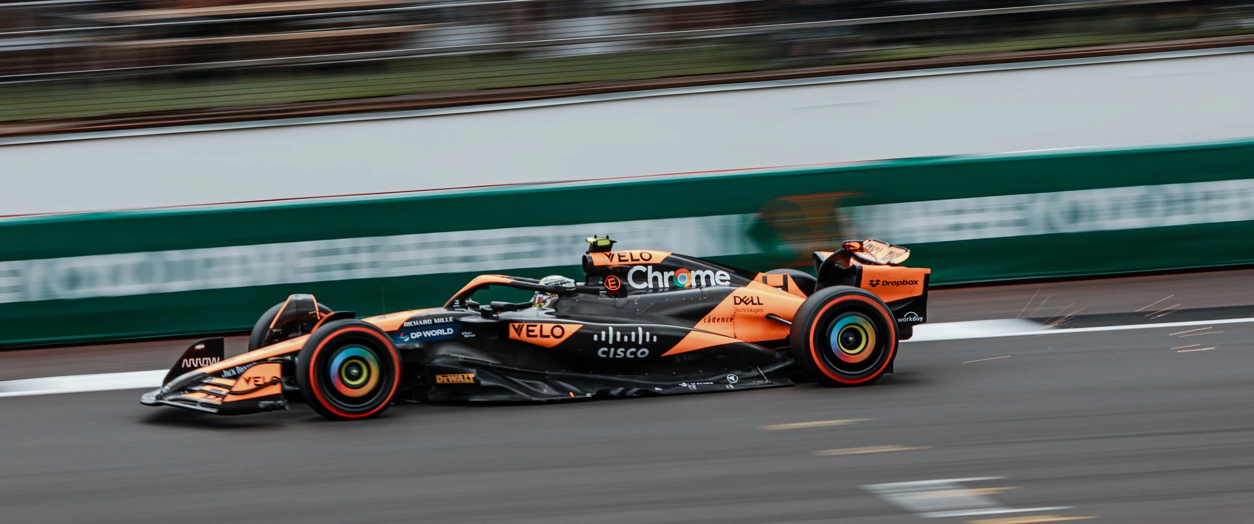 A Formula 1 race car on a track with sparks flying from the bottom, featuring orange and black colors and various sponsor logos.