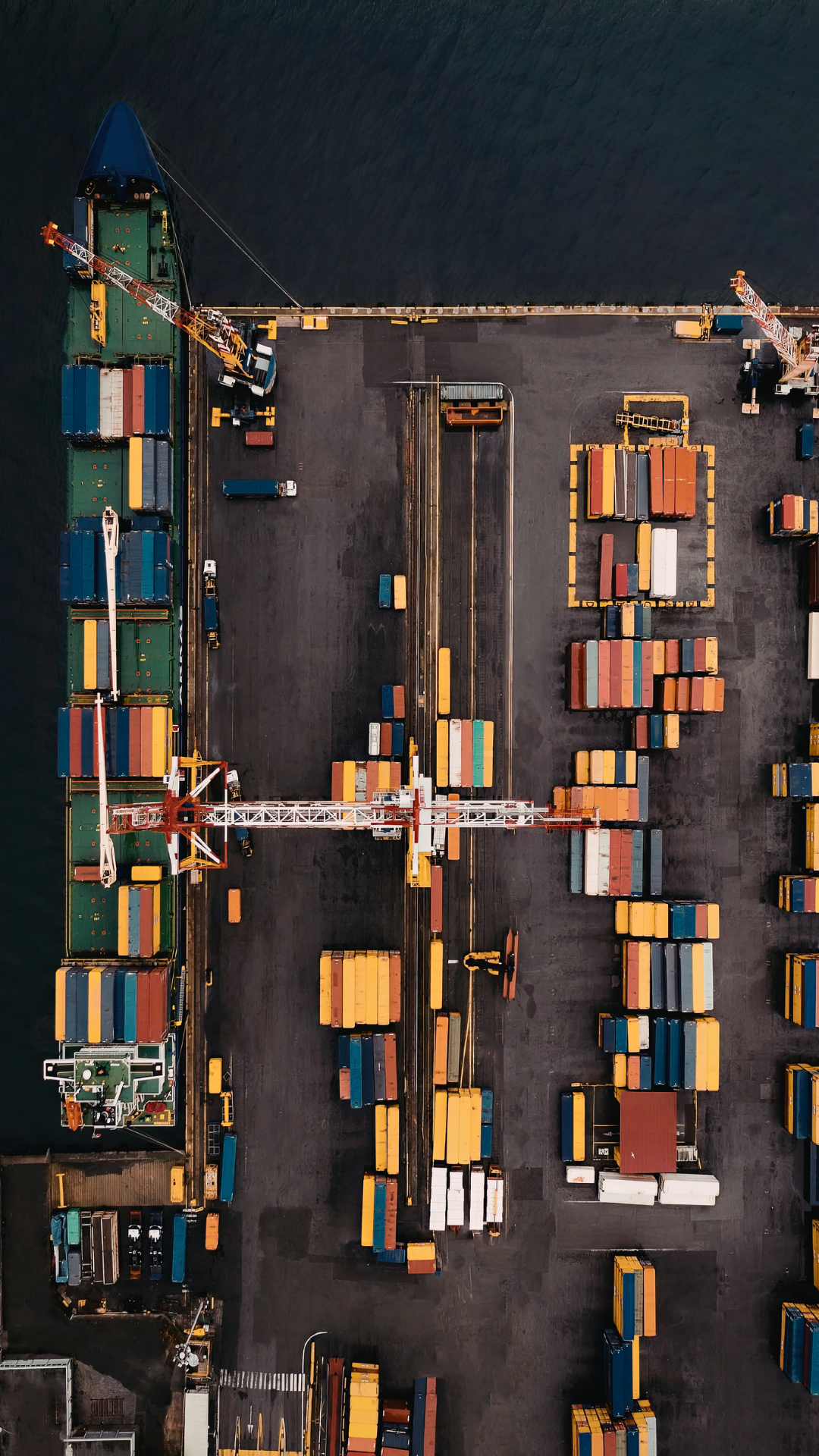 Aerial view of a shipping container yard with containers, cranes, and trucks.