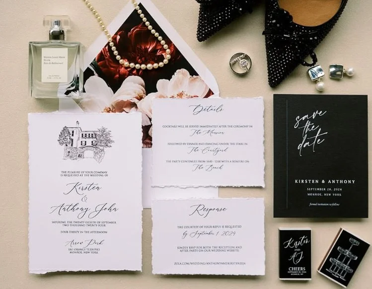 Wedding invitation suite with details for Kirsten and Anthony John, save the date card, response card, and additional stationery, surrounded by jewelry, perfume, and accessories on a neutral background.