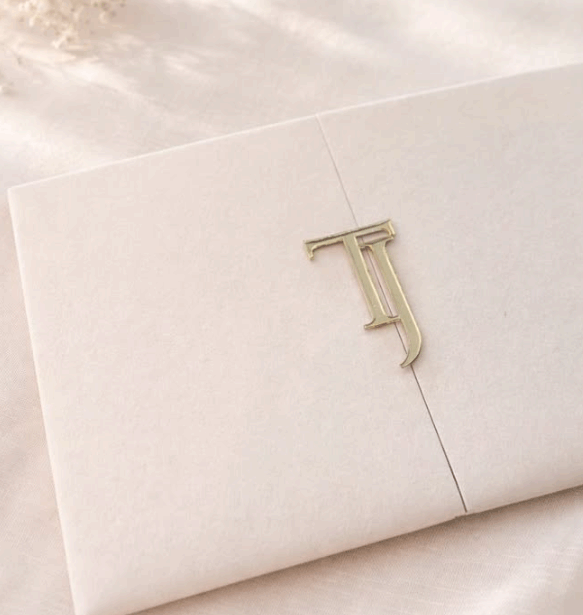 A white envelope secured with a decorative gold letter 'T' seal on a light fabric surface.