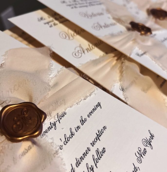 Close-up of wedding or event invitations with gold wax seals and elegant calligraphy, partially visible text.