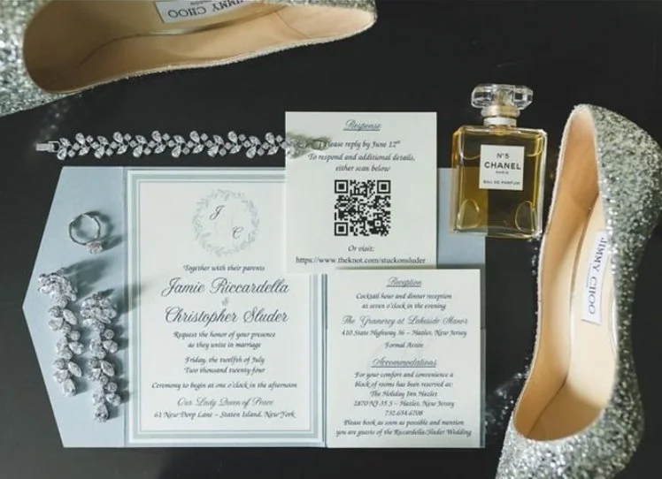Wedding invitation, Chanel perfume, a pair of high heels, and jewelry arranged on a table.