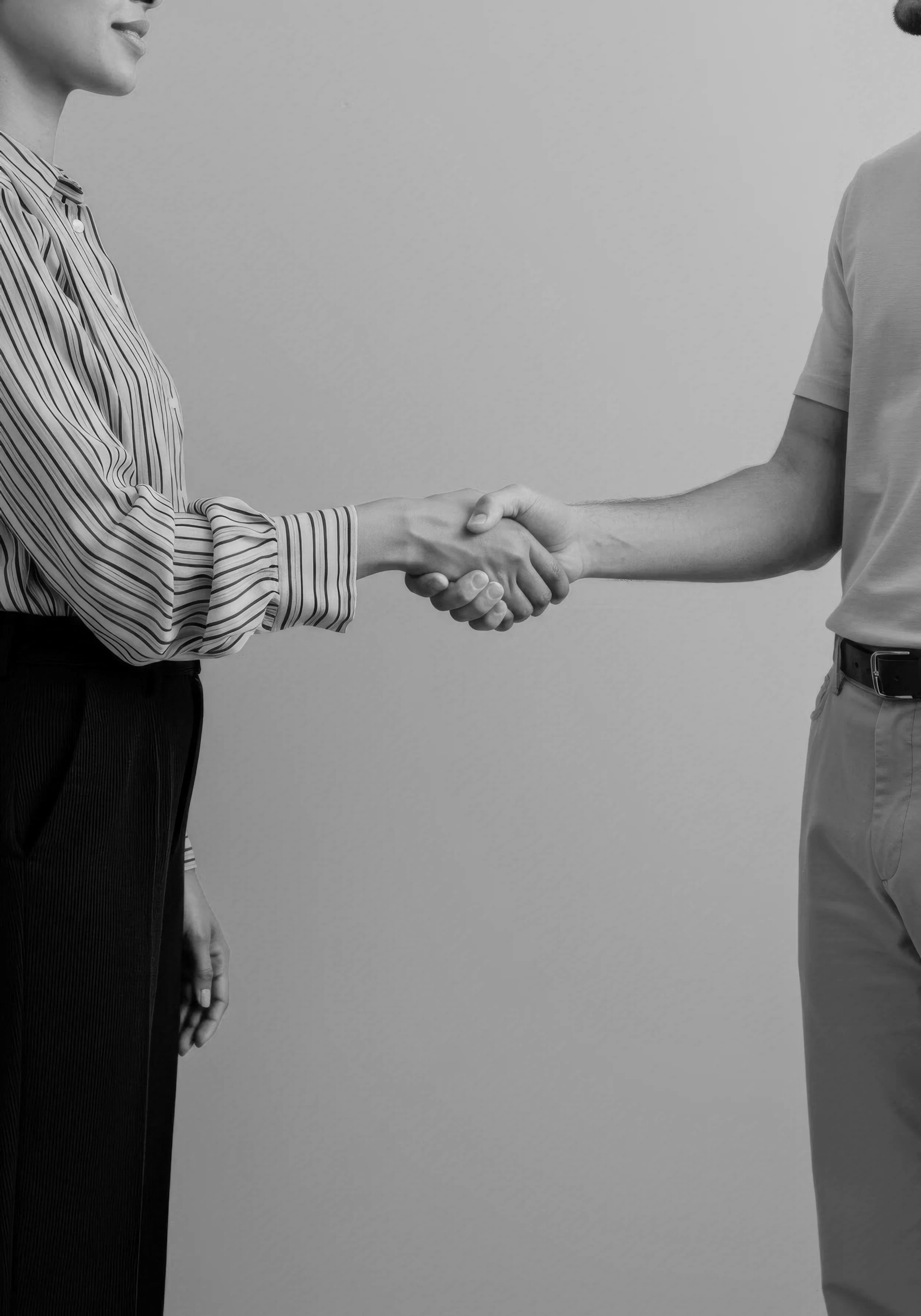 Black and white photo of two people shaking hands, with their torsos and arms visible, against a plain background.