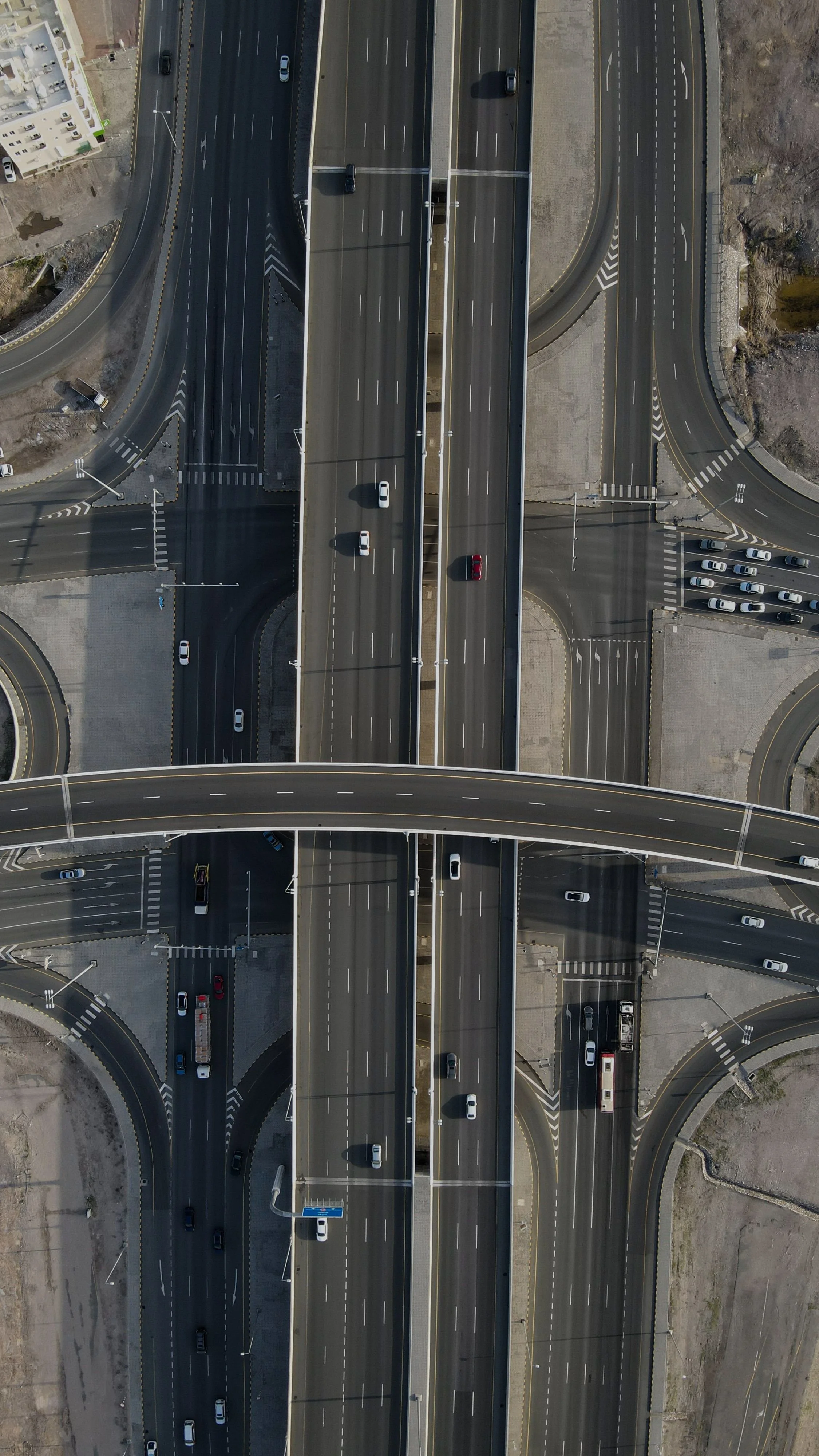 Aerial view of a multi-level highway interchange with multiple lanes, bridges, and ramps, with several cars traveling on the roads.