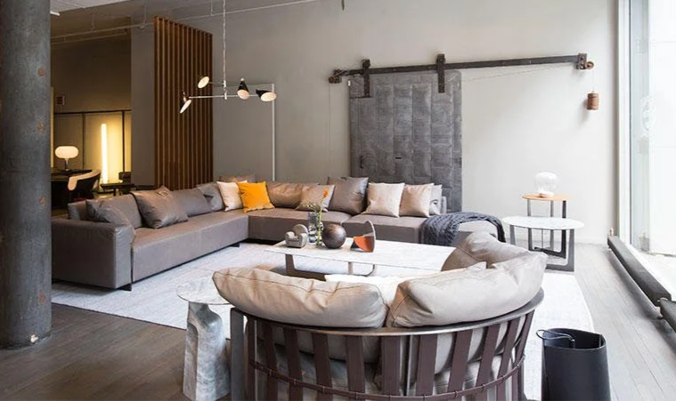 Modern living room with a large gray sectional sofa, a round leather armchair with beige cushions, a marble coffee table, and a sliding industrial door.