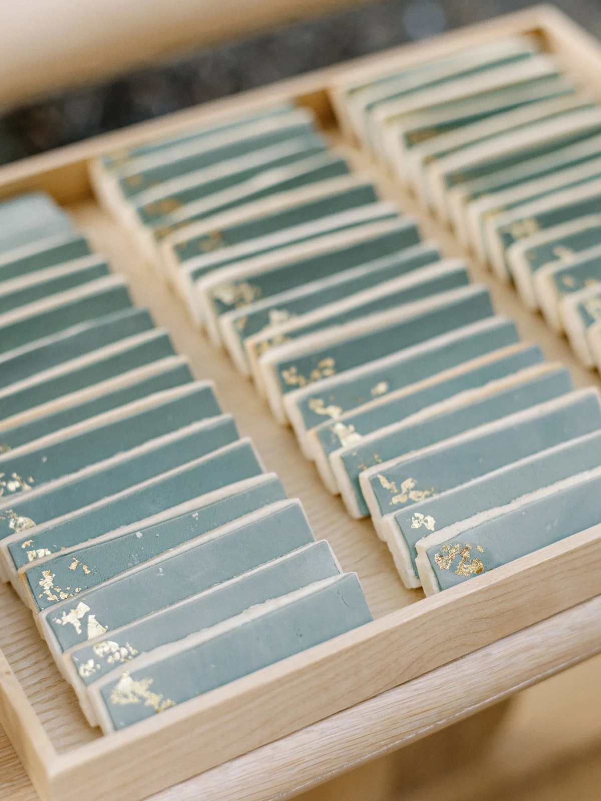 A wooden box containing multiple rectangular tiles with blue glaze and gold leaf accents.
