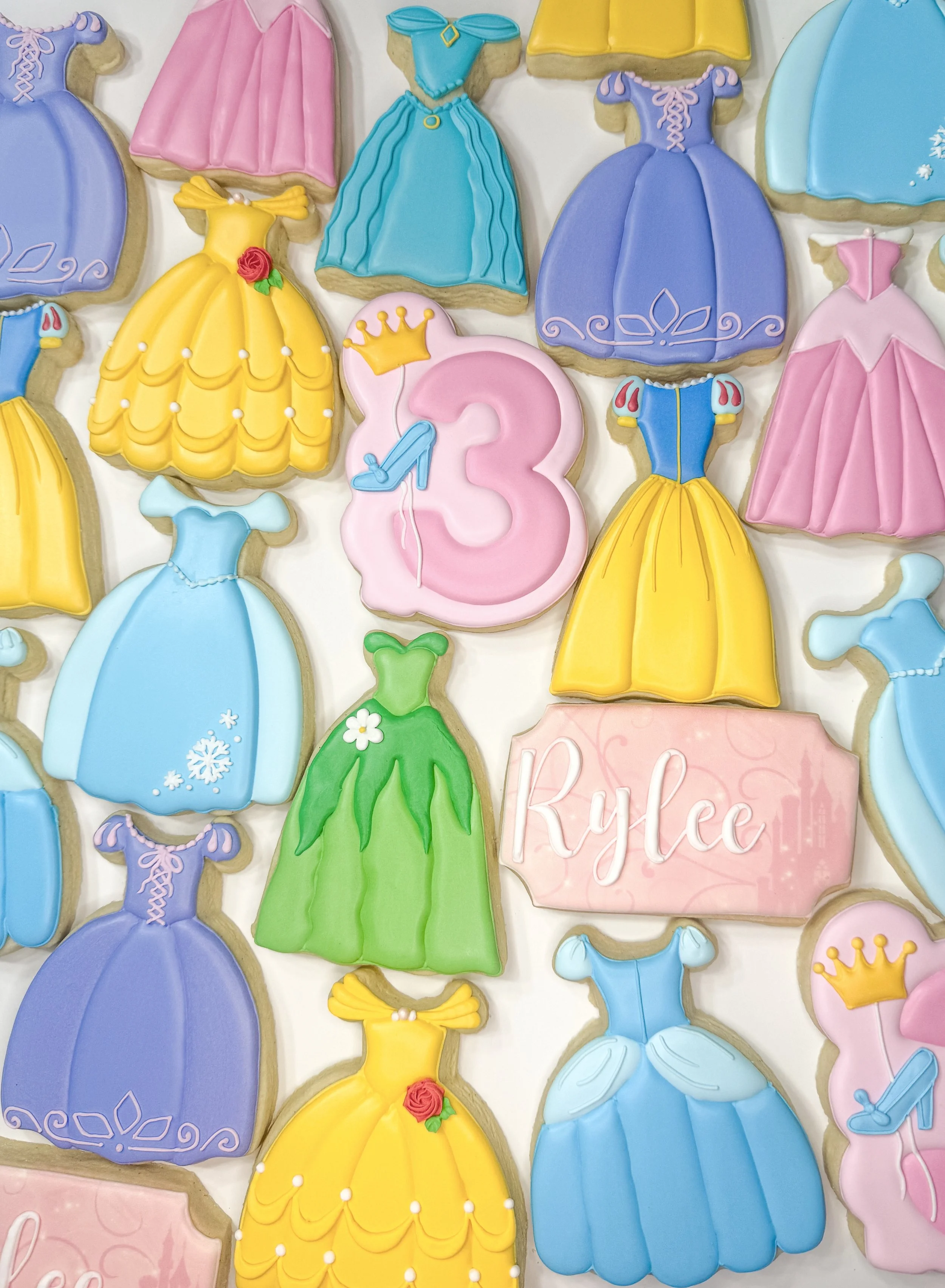 Array of decorated princess-themed cookies, including dresses, shoes, a castle, a crown, and a pink sign with the name 'Kylie'