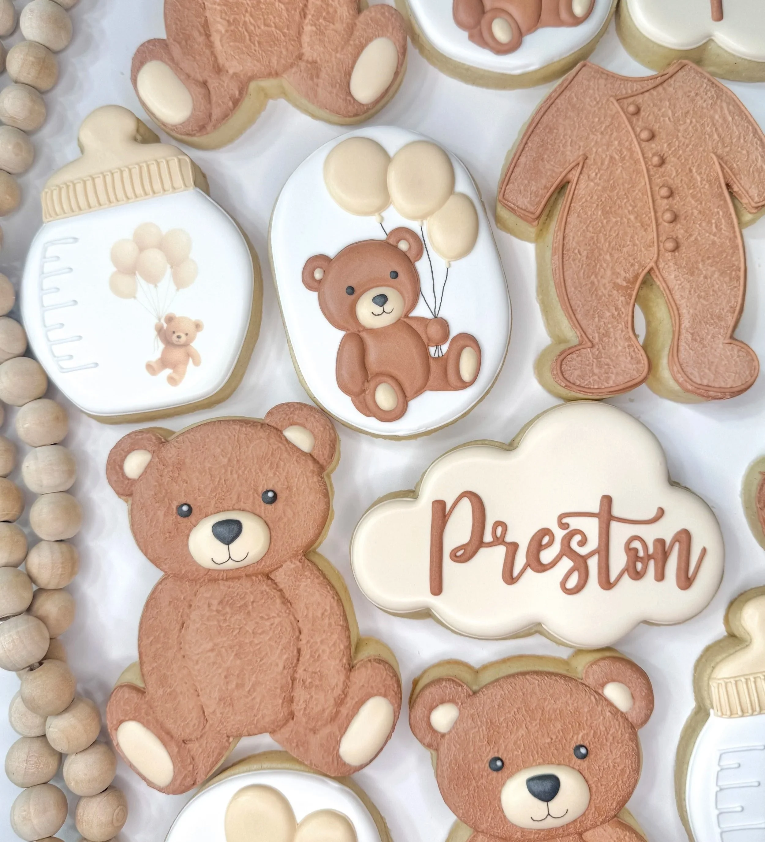 Decorative cookies with teddy bear, baby bottle, and balloon designs surrounded by beige beads.