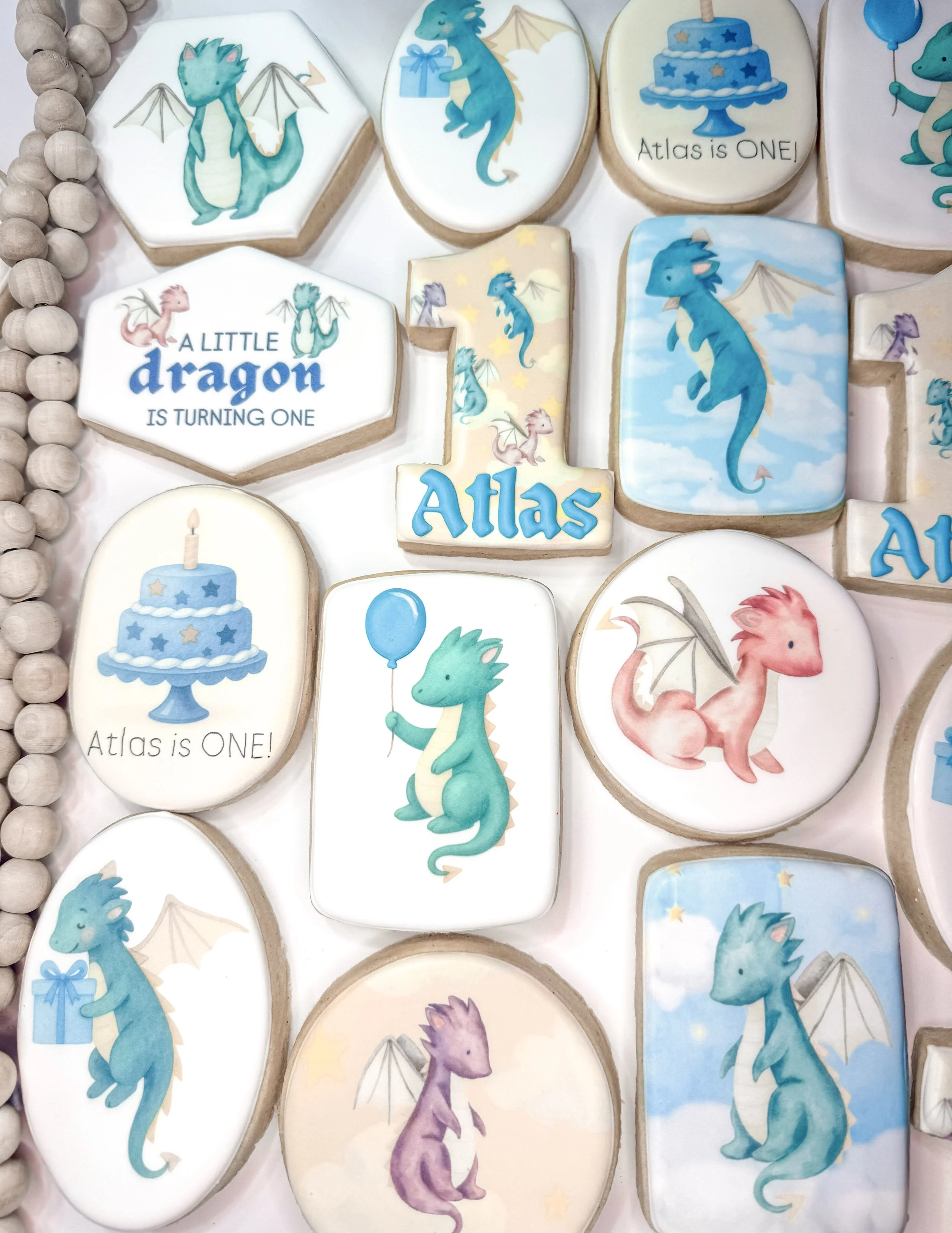 Decorative cookies featuring dragons, birthday cake, balloons, and text celebrating a child's first birthday and their name Atlas.