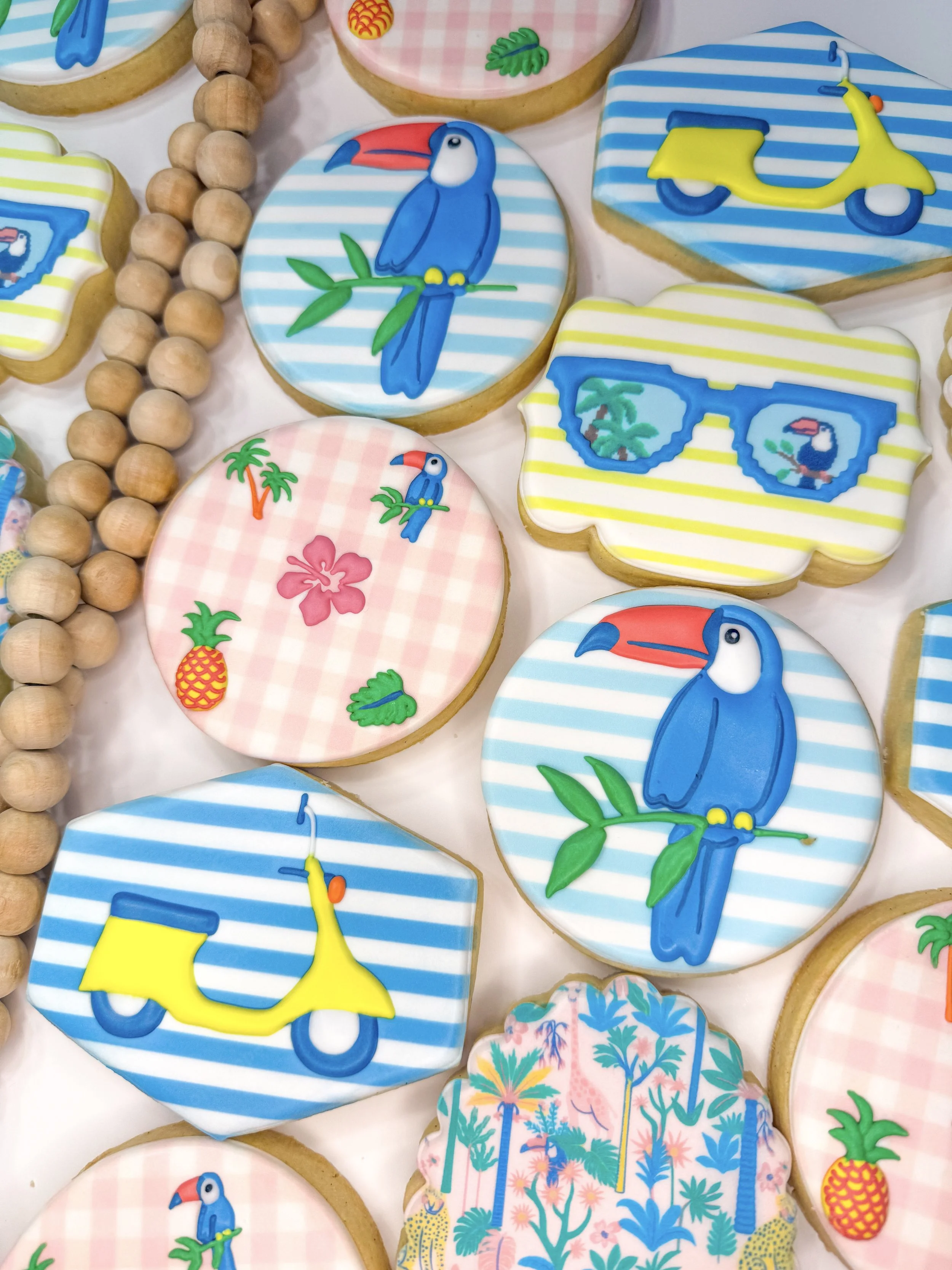 Decorative cookies with tropical and beach themes, including toucans, scooters, pineapples, palm trees, and colorful patterns.