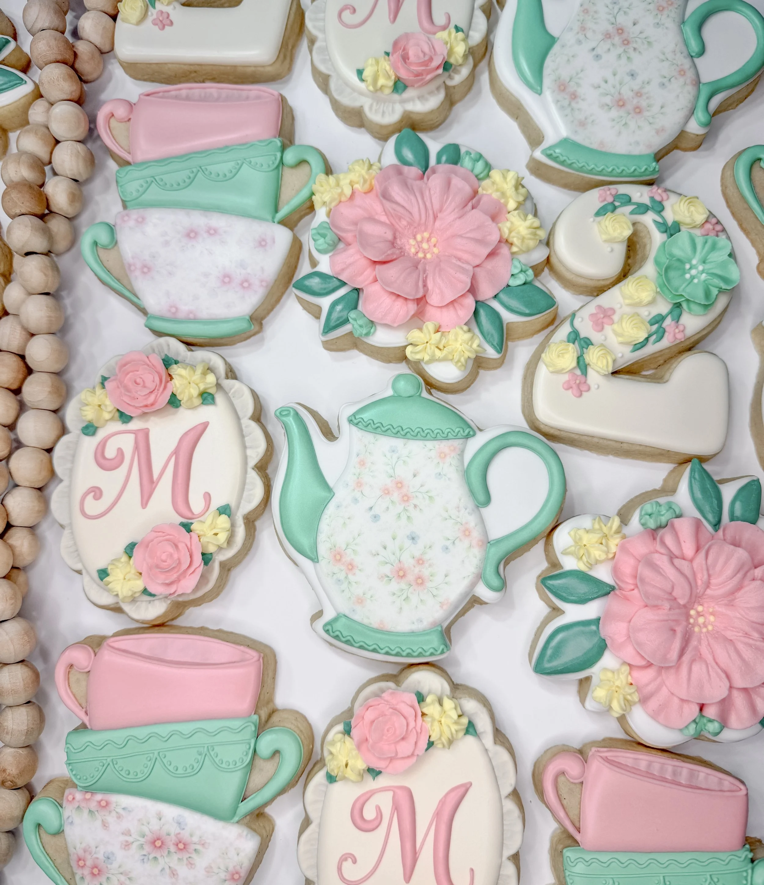 Assorted decorated cookies with floral, teapot, teacup, and pink-themed designs.