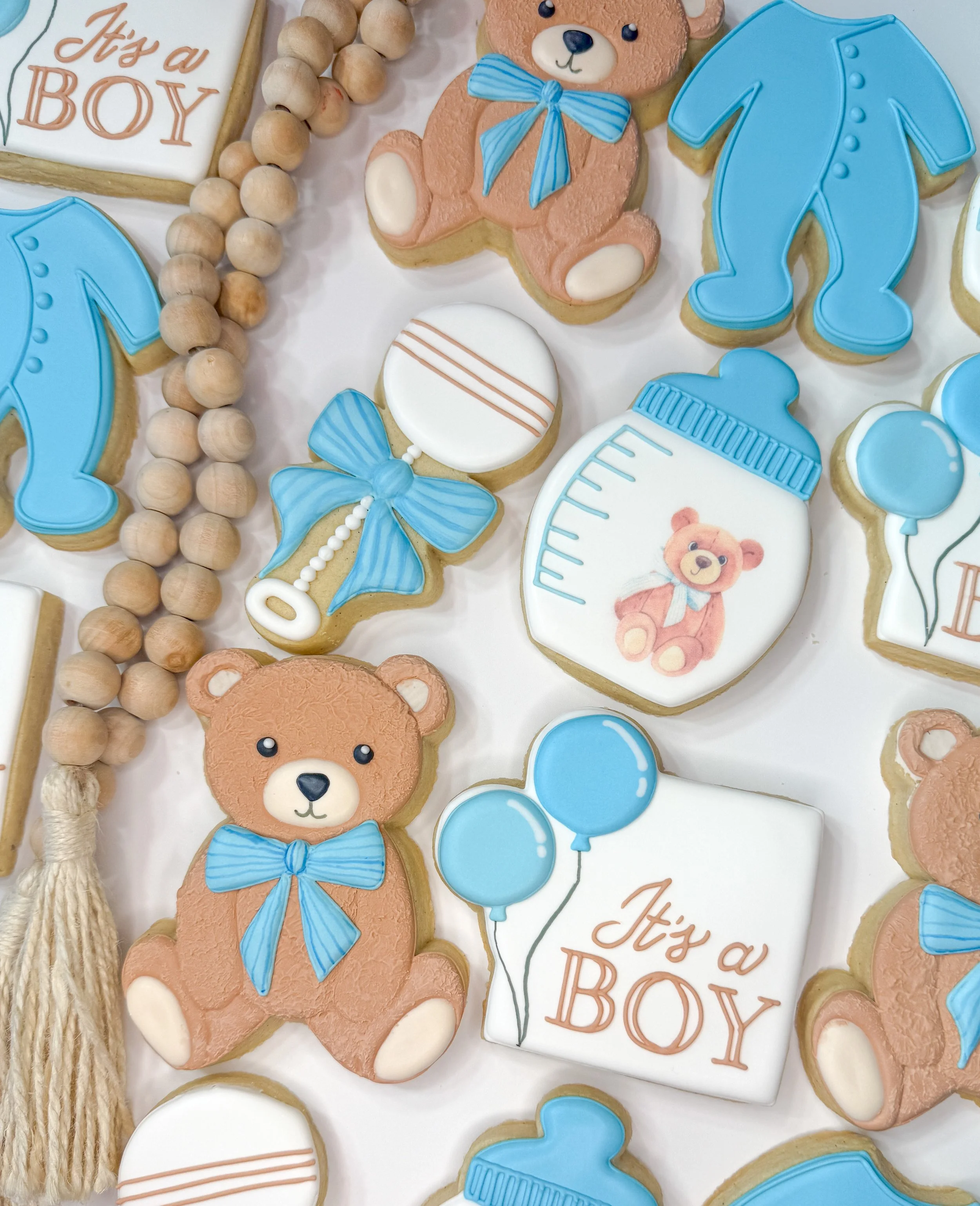 Baby shower cookies decorated with teddy bears, blue ribbons, balloons, a baby bottle, and a message that says 'It's a Boy'.