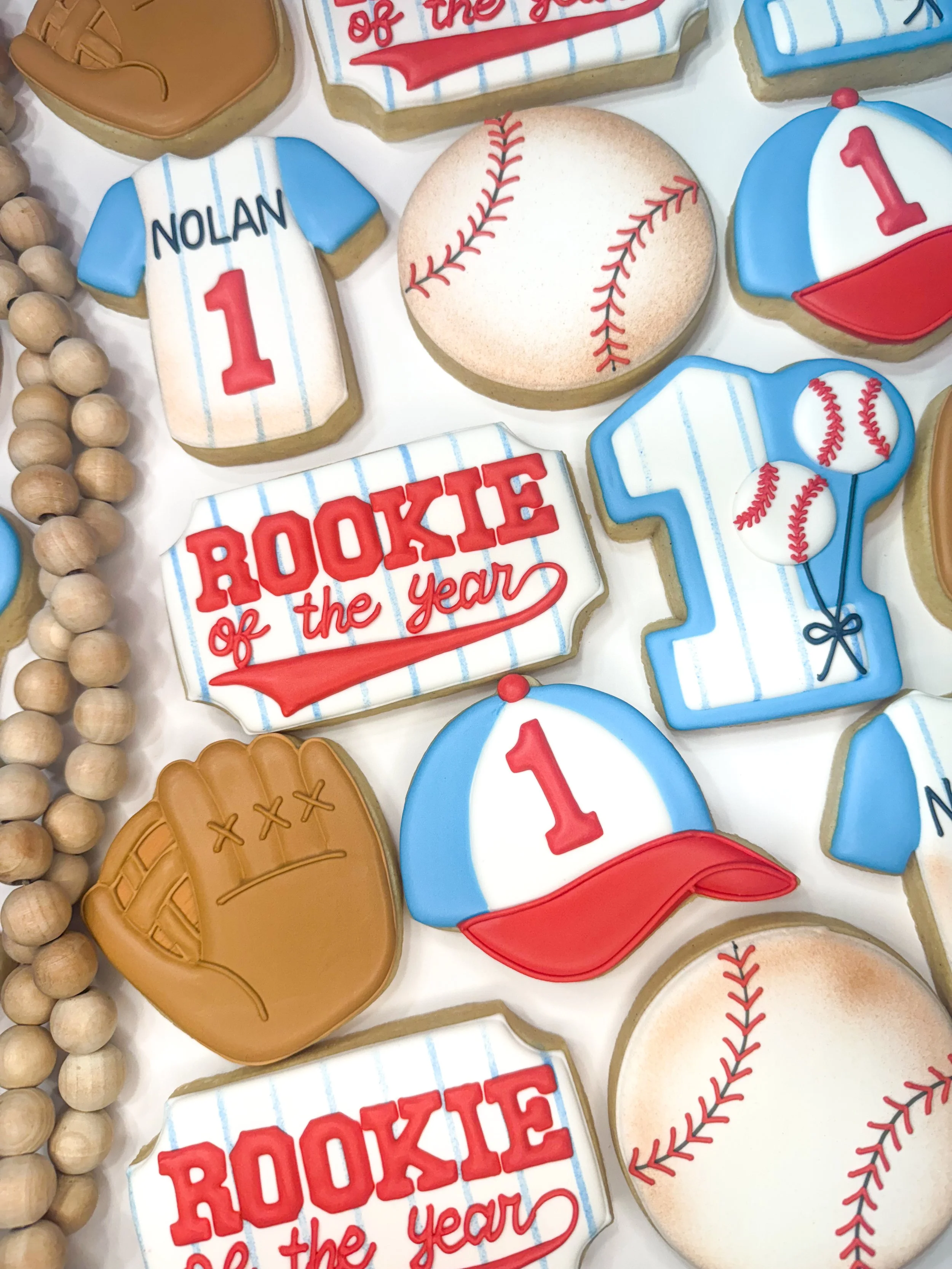 Decorative cookies with baseball-themed designs, including a baseball, a baseball cap, a baseball glove, a baseball jersey with the name Nolan and number 1, and phrases like 'Rookie of the Year'.