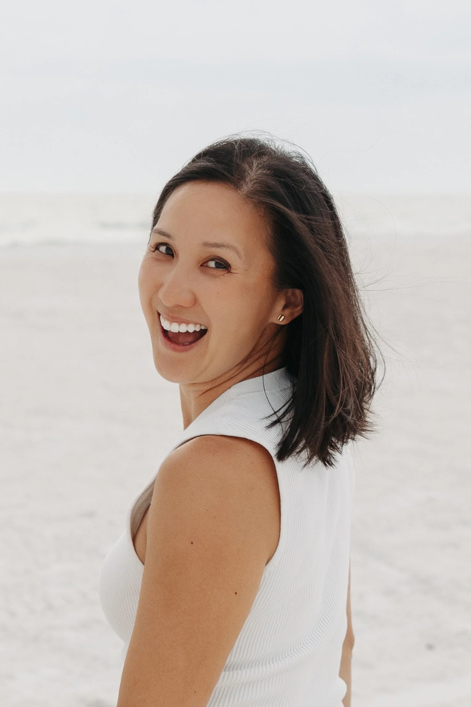 Close-up of a woman smiling on a beach, with ocean waves in the background.