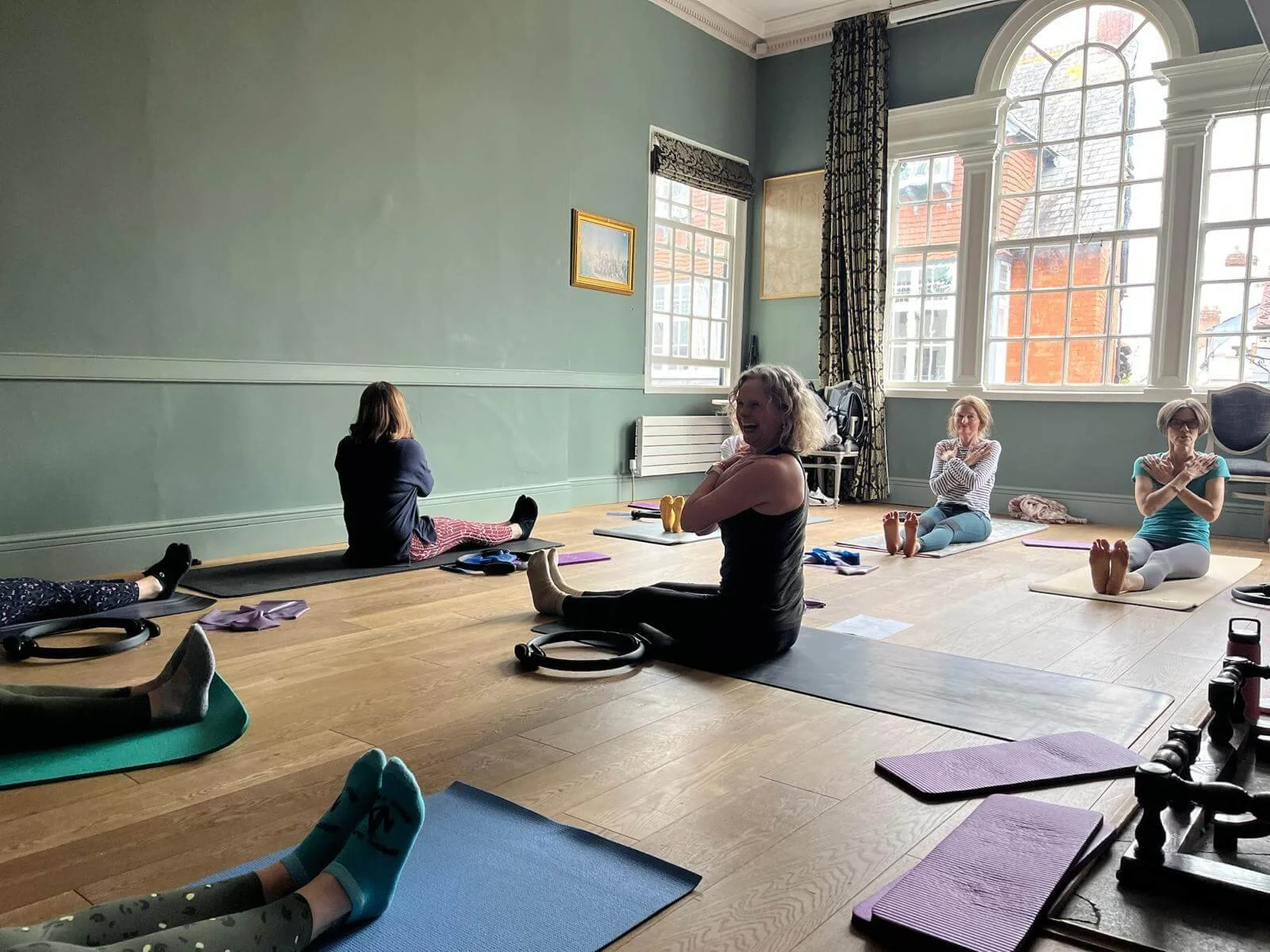 A group of women participating in a pilates class in Topsham a spacious room with large windows and green walls at exe Valley Pilates