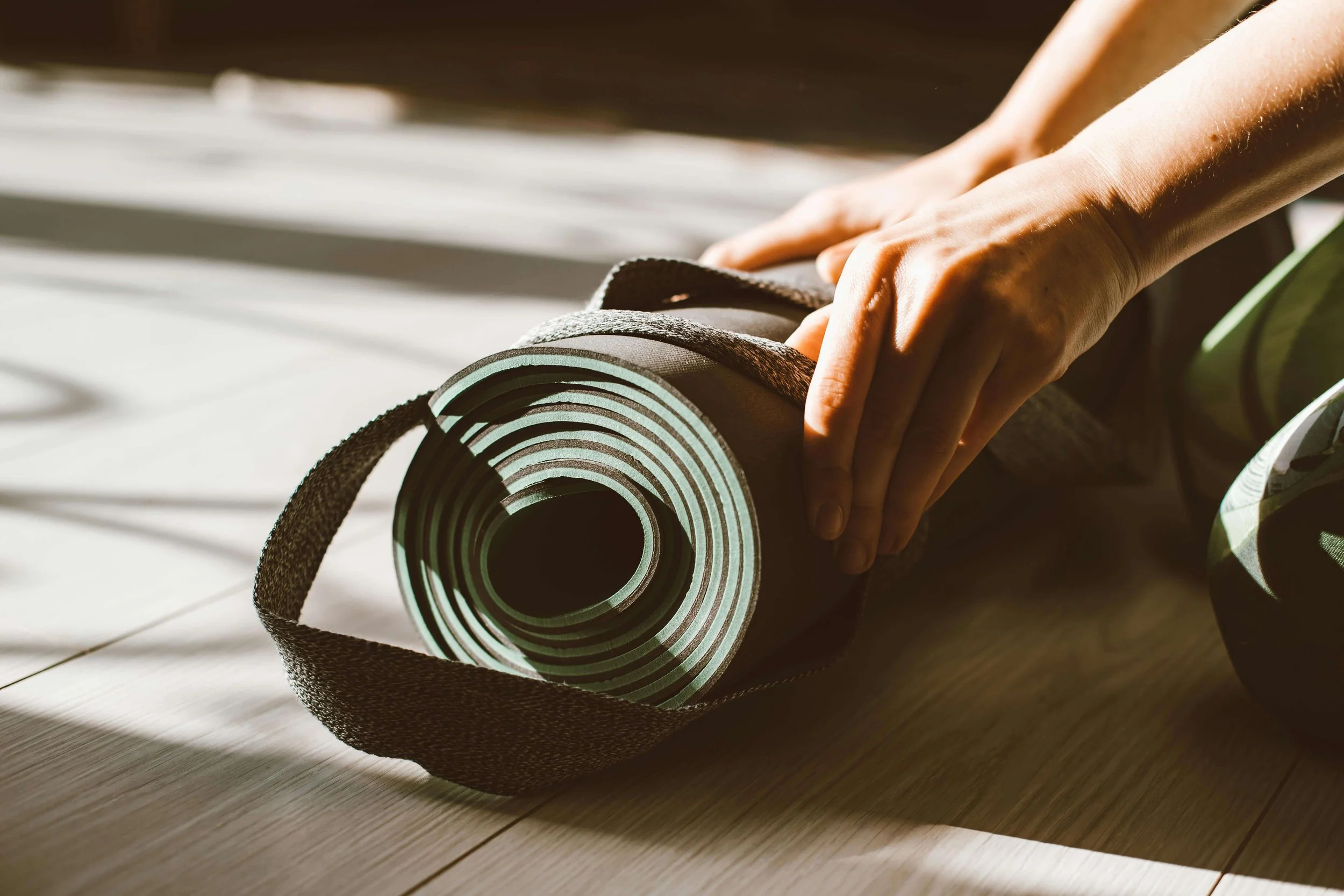 Someone unrolling a black pilates mat on a wooden floor.