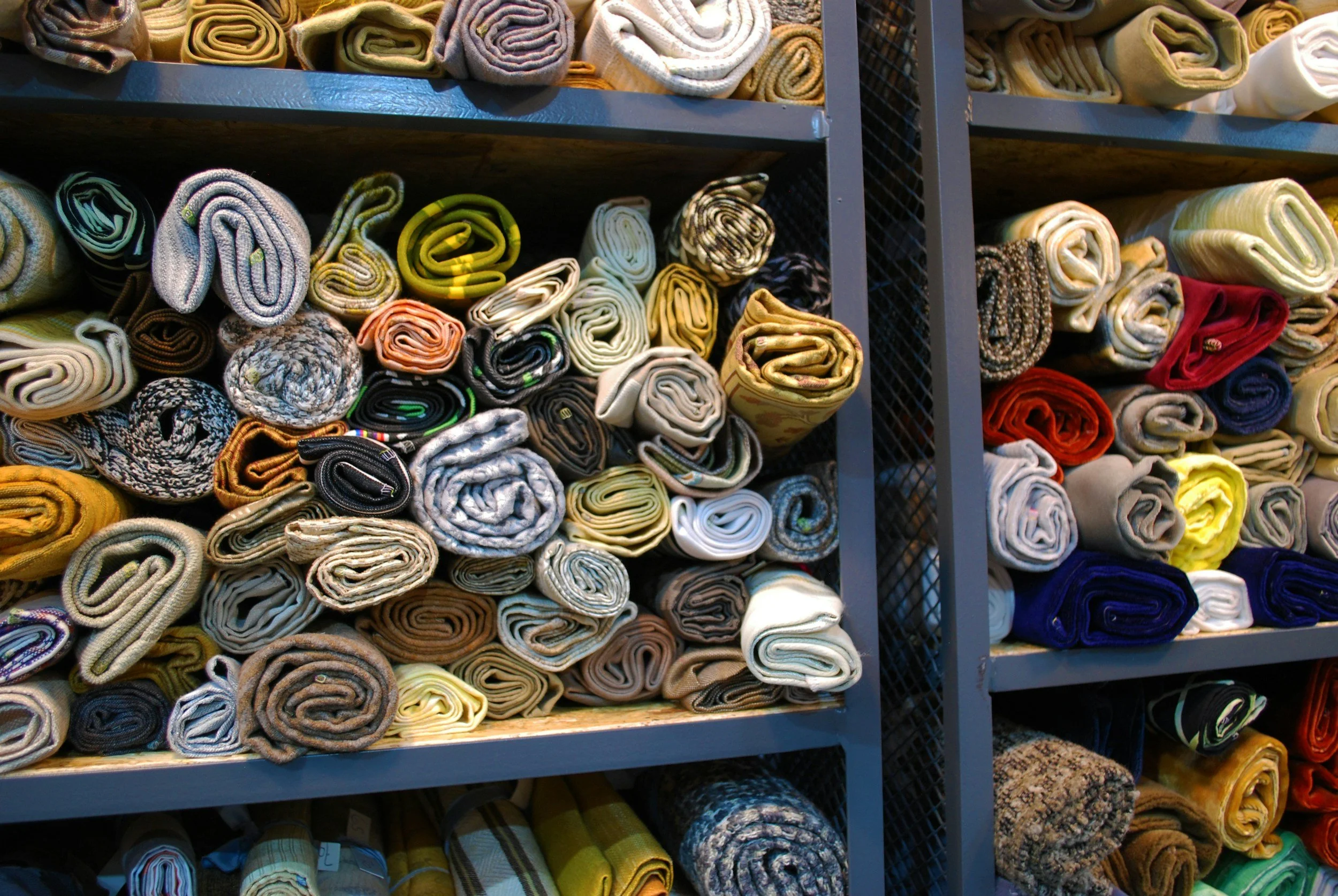 Stacks of rolled-up towels in various colors organized on metal shelves in a store.