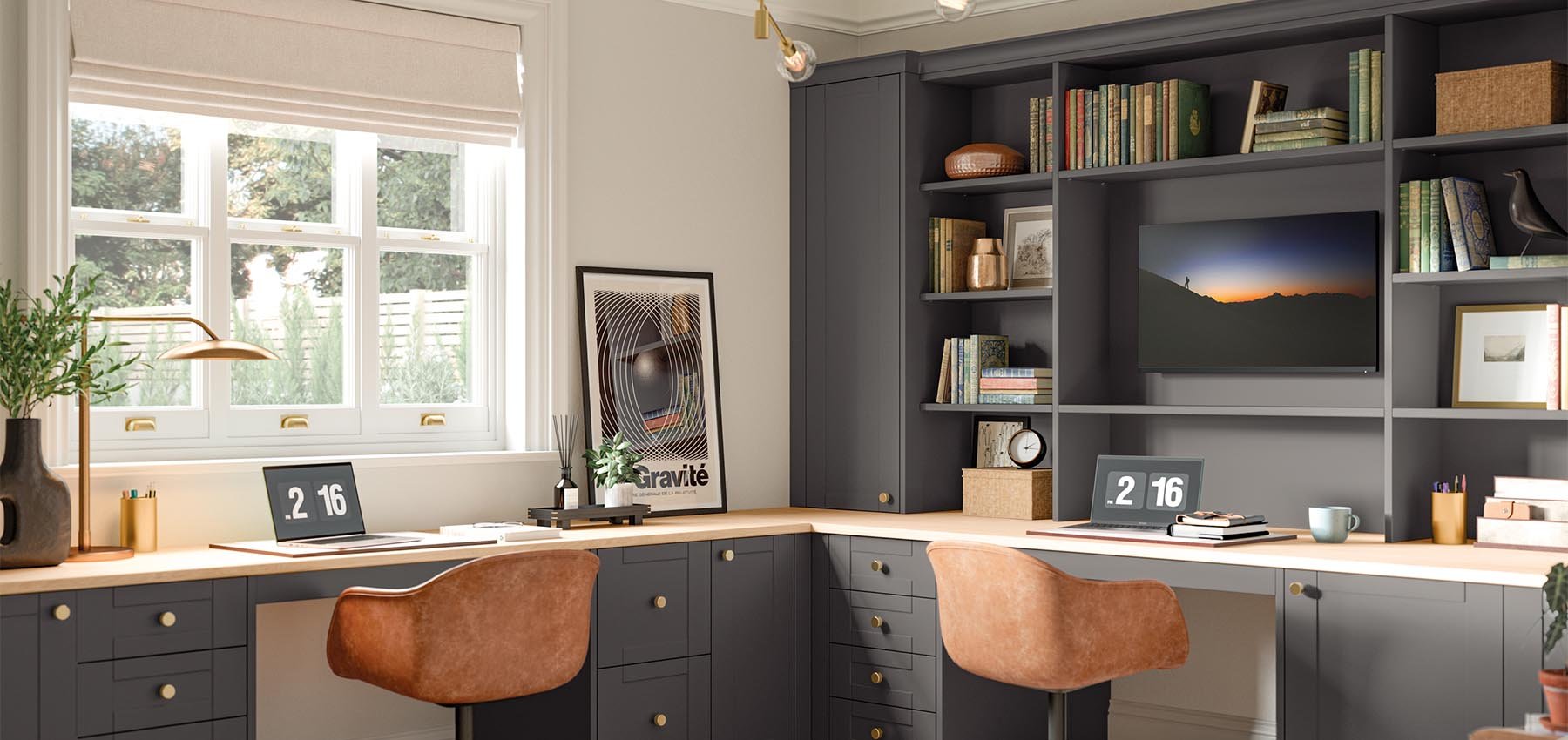 Home office with two workstations featuring laptops, decorative items, books, and framed artwork, with a window overlooking greenery and a grey and beige color scheme.