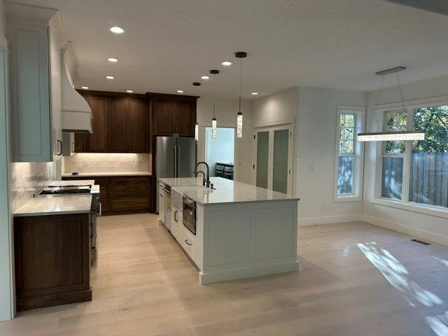 Contrasting cabinetry with layered island pendant and recessed lighting in a kitchen remodel