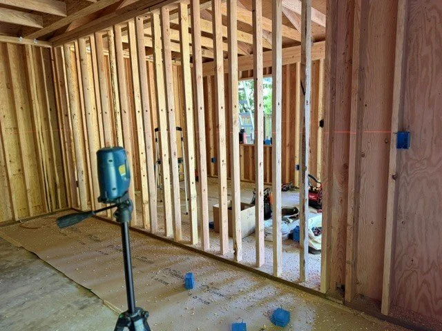 Electrician using a laser level during rough-in framing for a detached home office electrical build in Tigard, Oregon