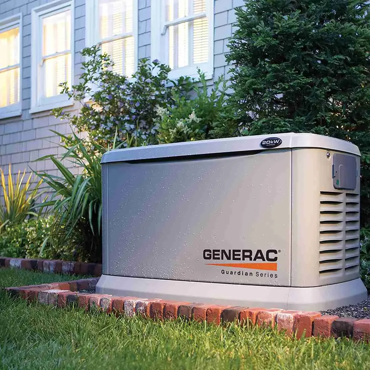 Generac Guardian Series standby generator installed outside a house with garden plants and shrubs in the background.
