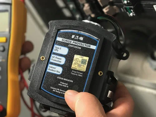 Close-up of a surge protector device being held in hand, labeled 'EATON Surge Protector' with technical specifications on the label
