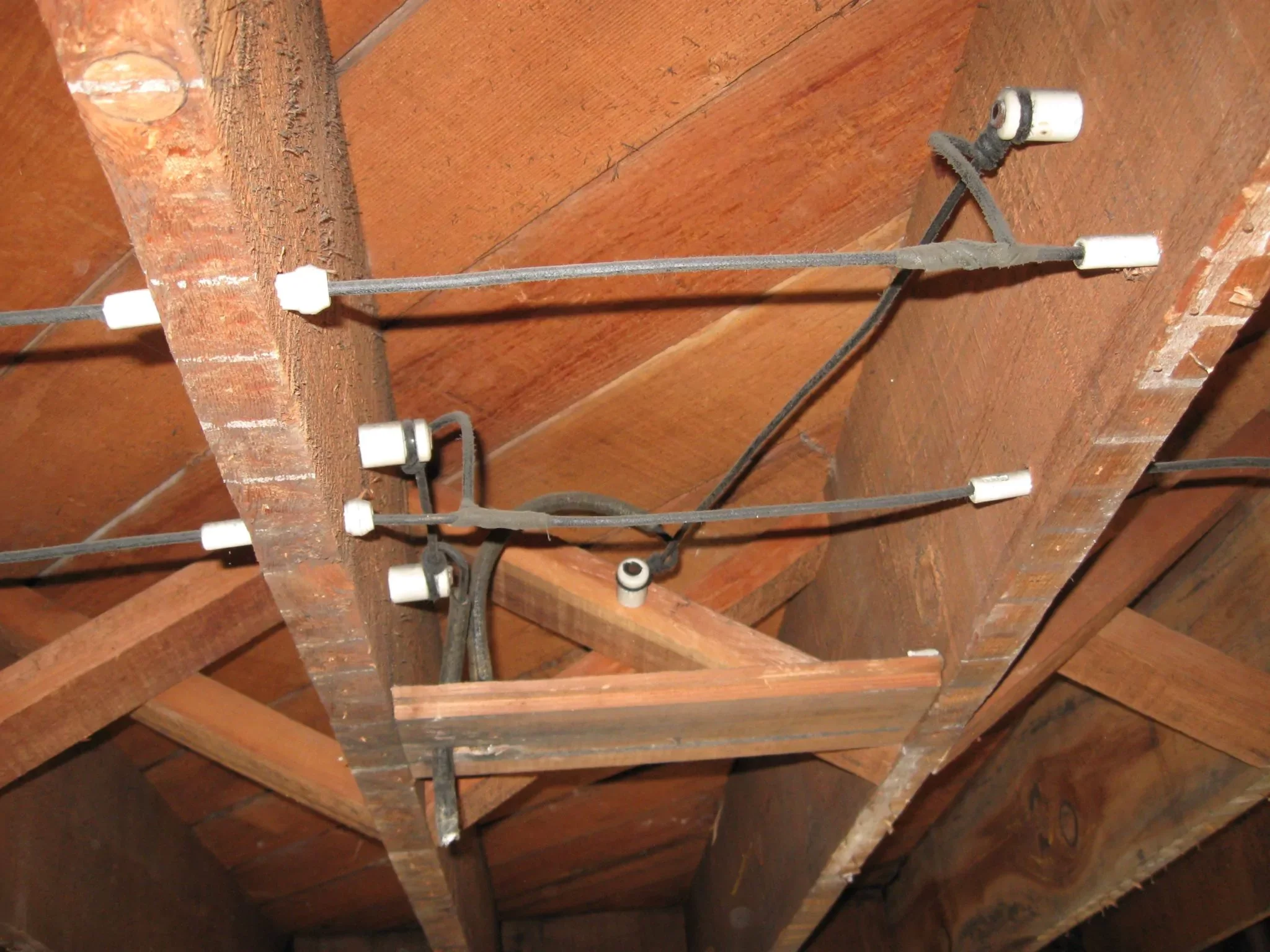 Electrical wires and ceramic insulators attached to wooden framing in a ceiling.
