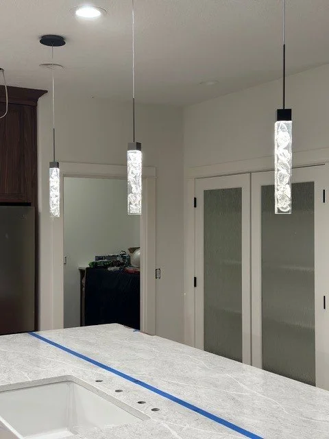 Close-up of textured glass cylinder pendant lights over a marble kitchen island during installation