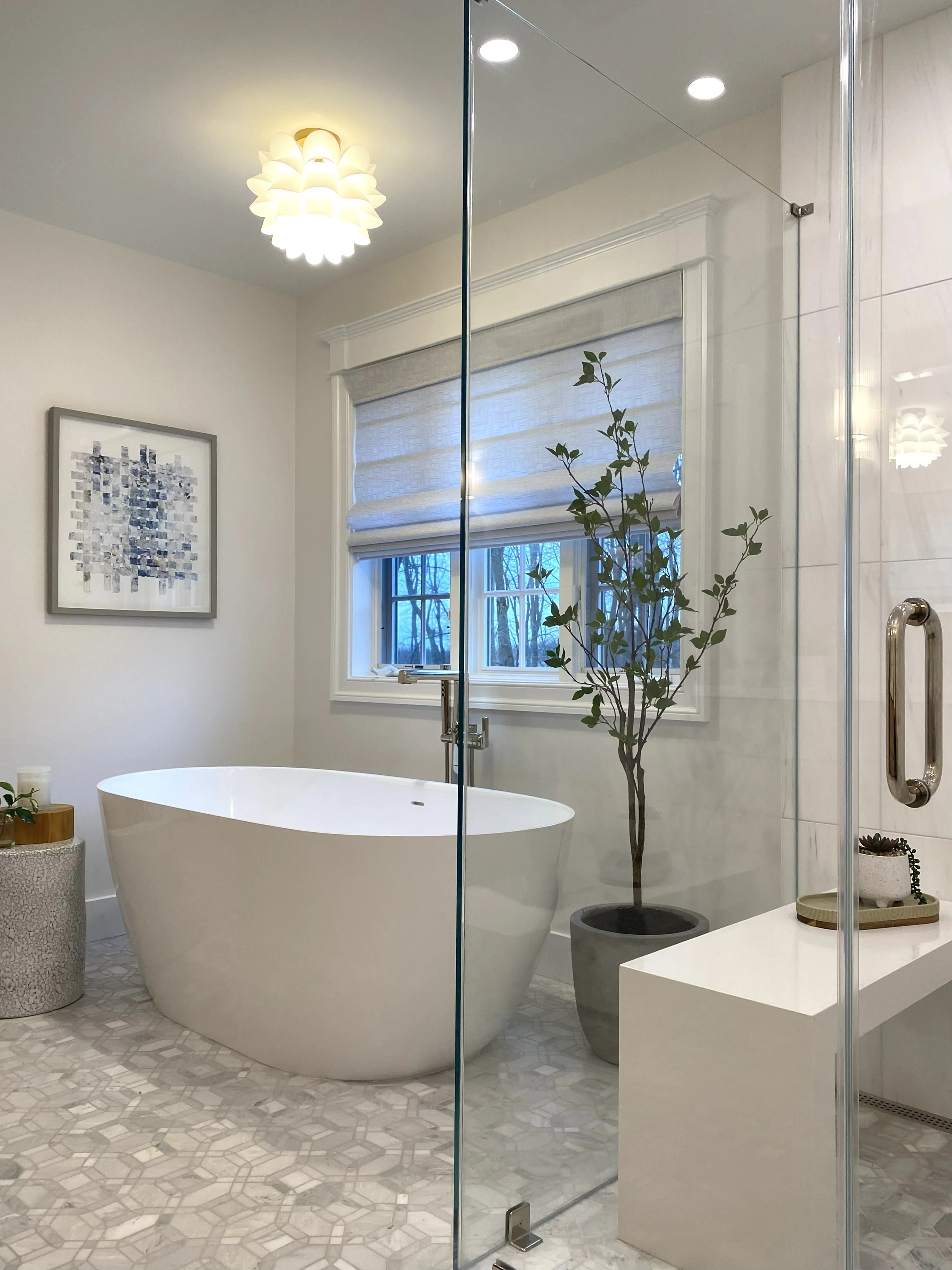 Modern bathroom with a standalone white bathtub, large window with blinds, potted plants, artwork on the wall, and a glass shower enclosure.