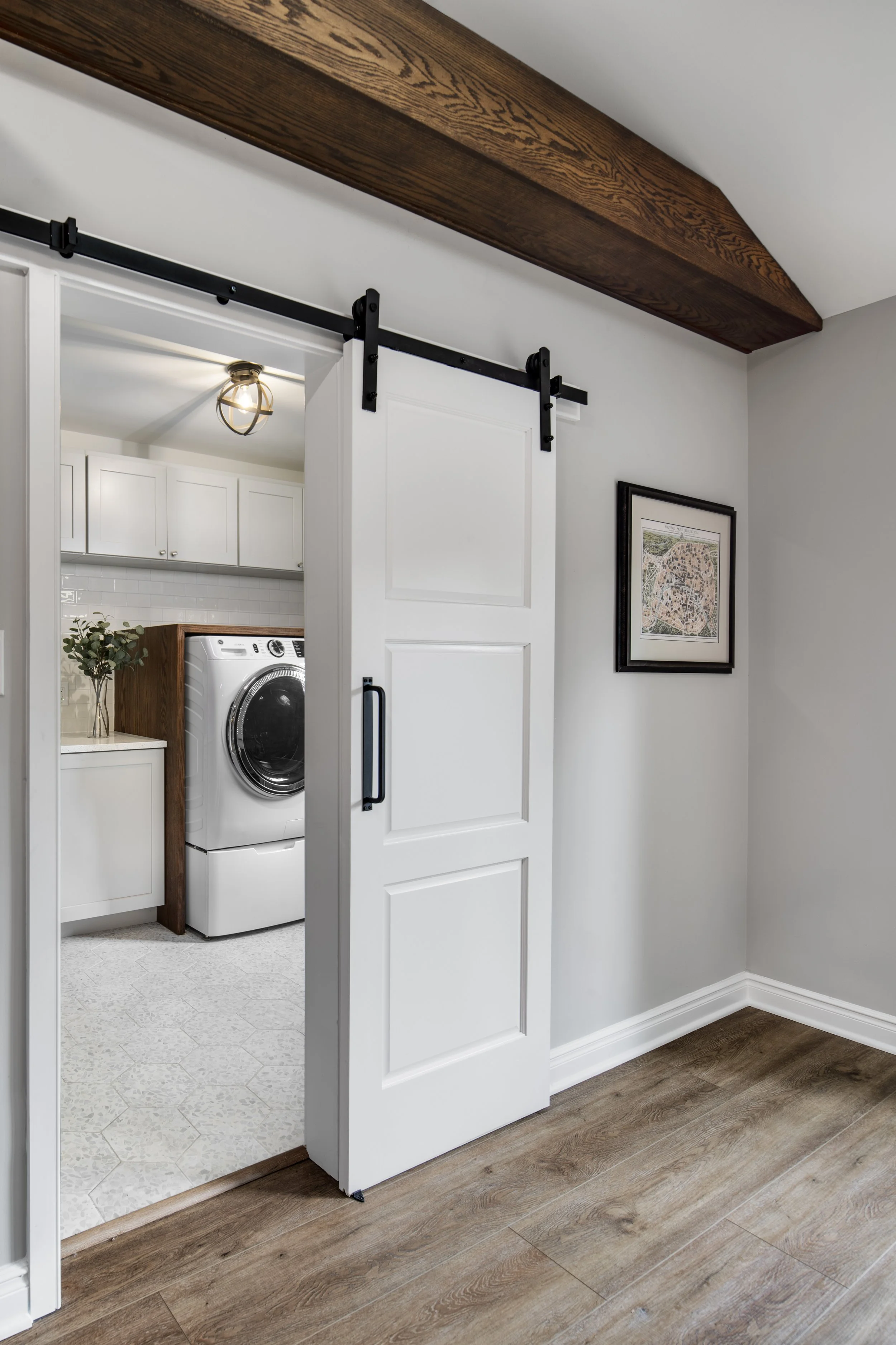 White sliding barn door open to laundry room with washer, cabinets, and decorative plant, above hardwood flooring.