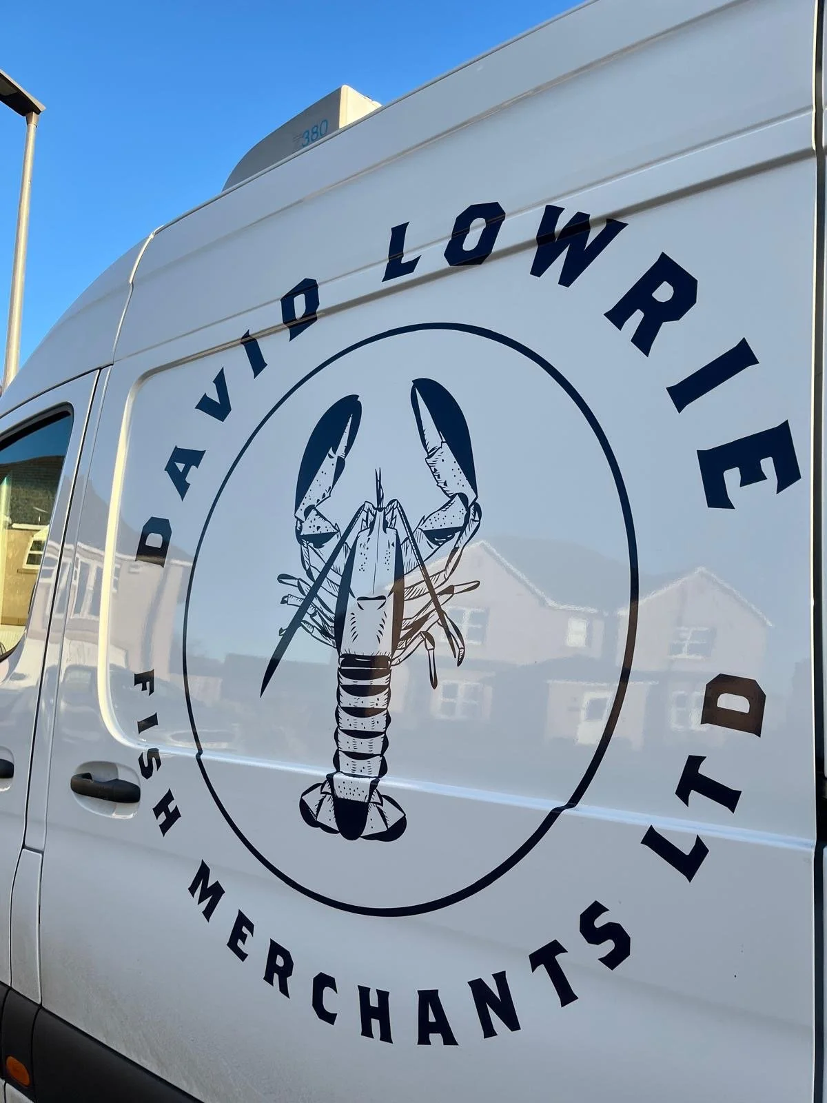 A white service van with a logo featuring a lobster holding fishing spears, and the text 'David Lowrie Shrimp Merchants' around the lobster.