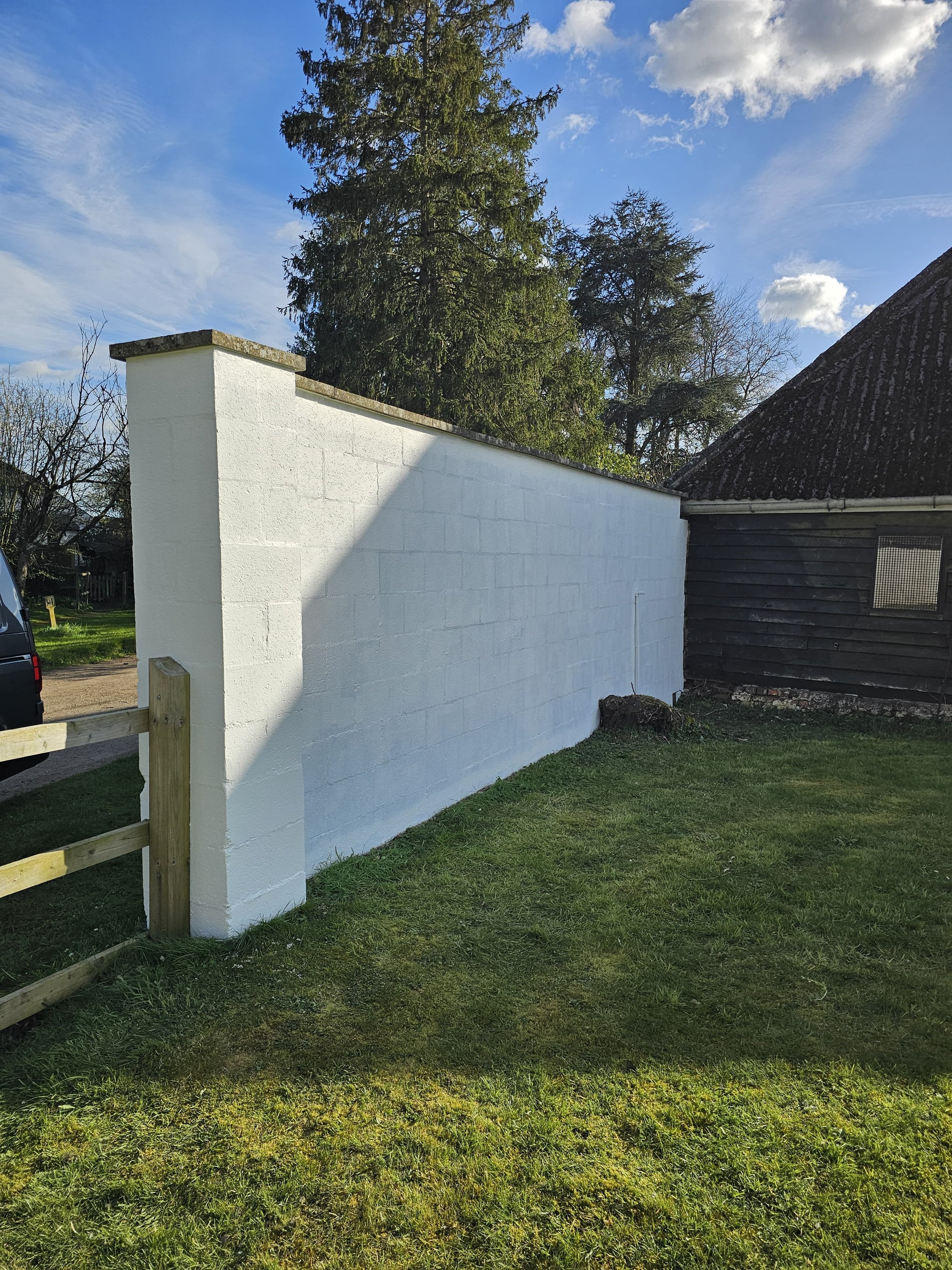 A newly white painted brick wall next to a black wooden building