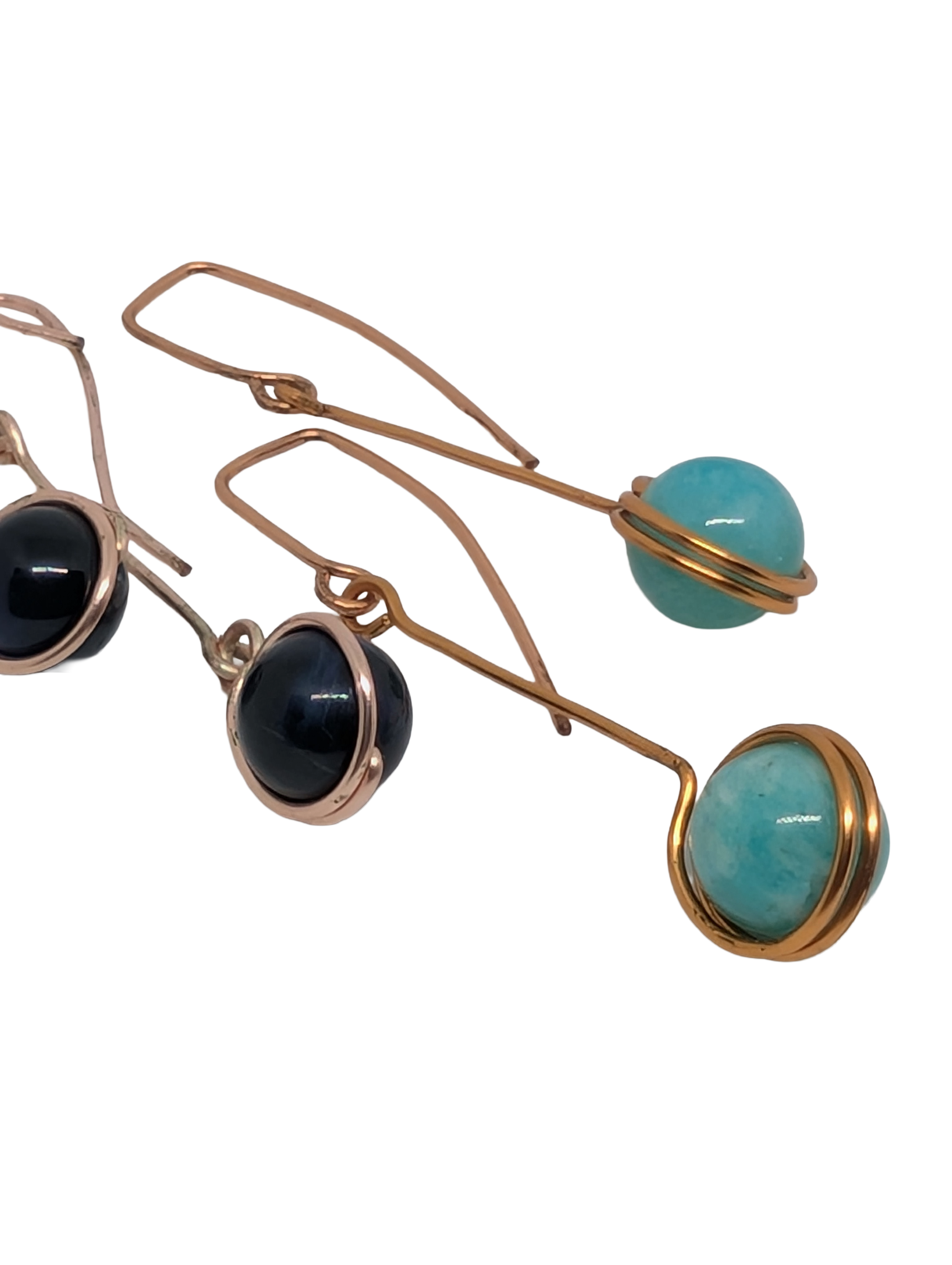Close-up of several wire hoop earrings, some with black or turquoise stones, on a white background.