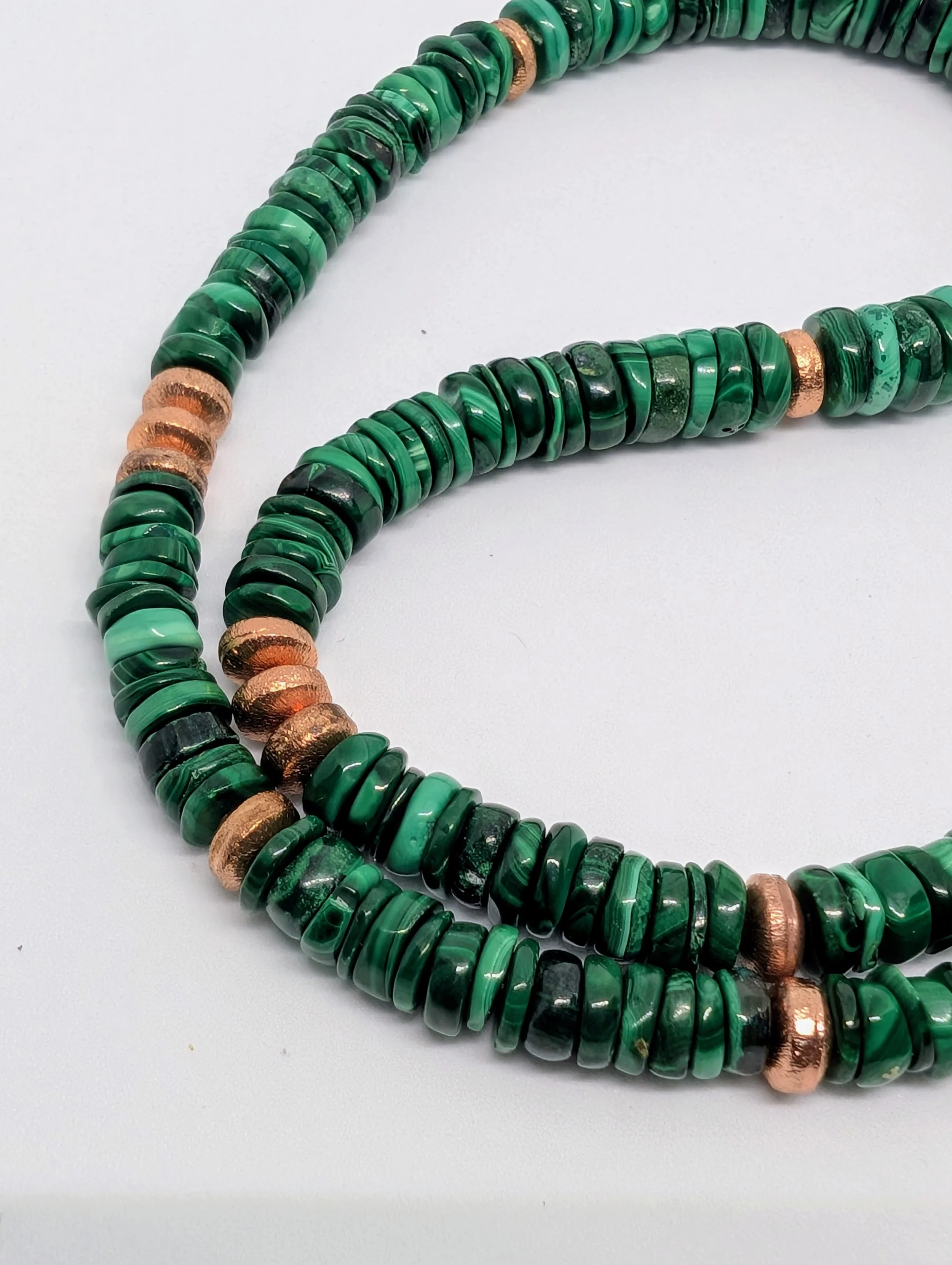A close-up of a beaded necklace made of green stone or glass beads with some copper-colored beads interspersed.