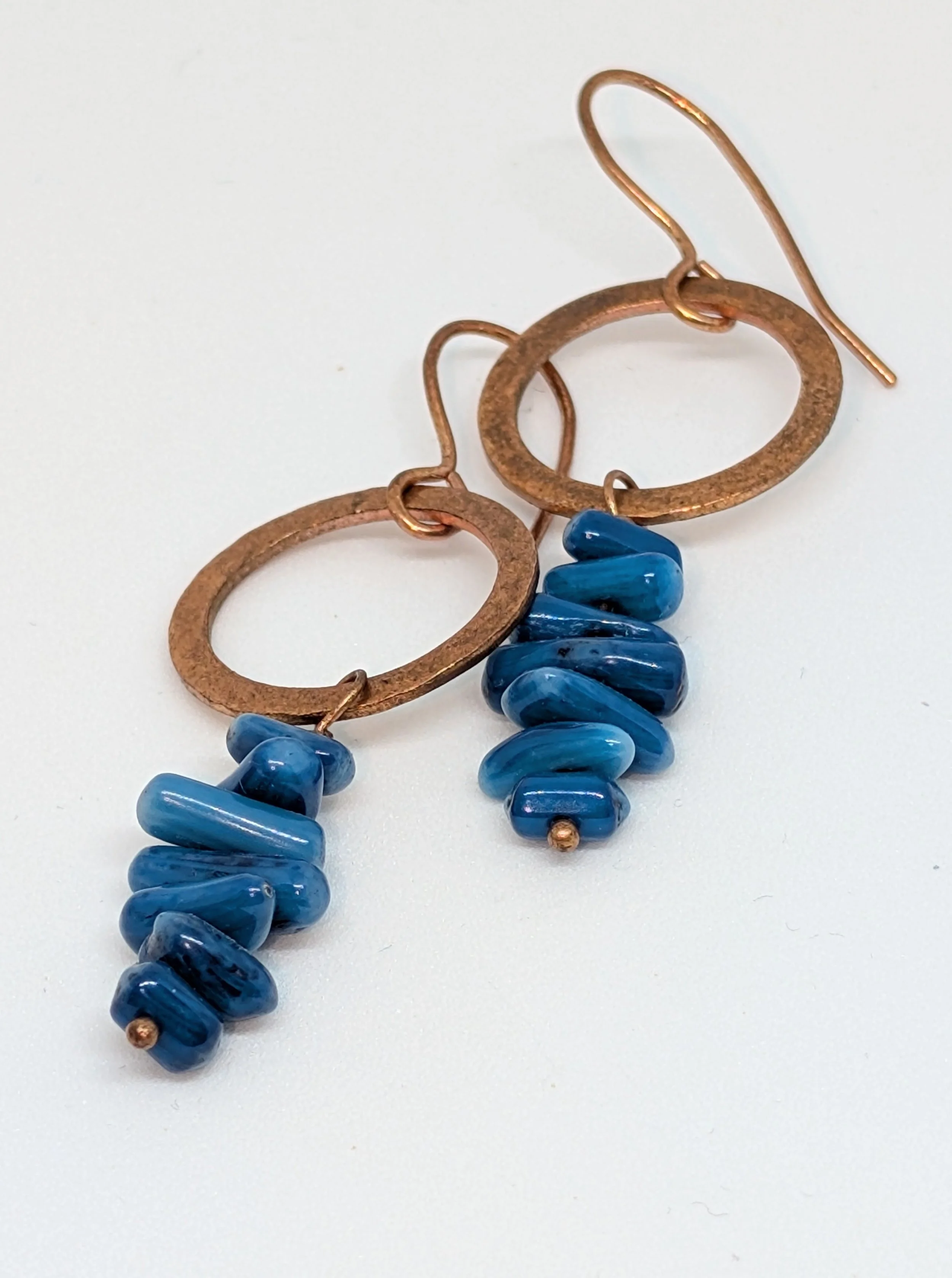Close-up of a pair of earrings with large copper hoops and blue glass beads, on a white background.