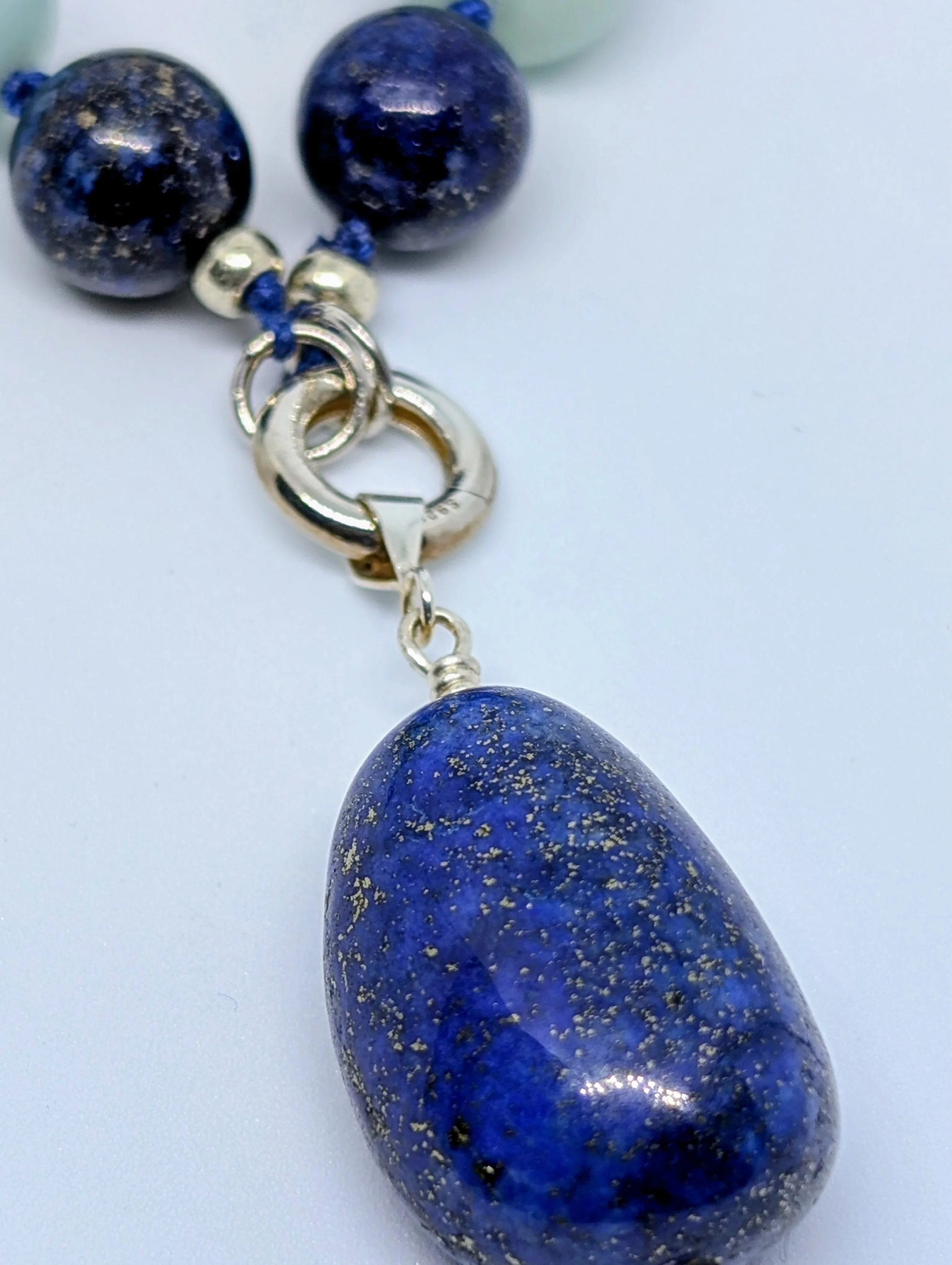 Close-up of a blue, speckled stone with a silver clasp, part of a necklace or jewelry piece.