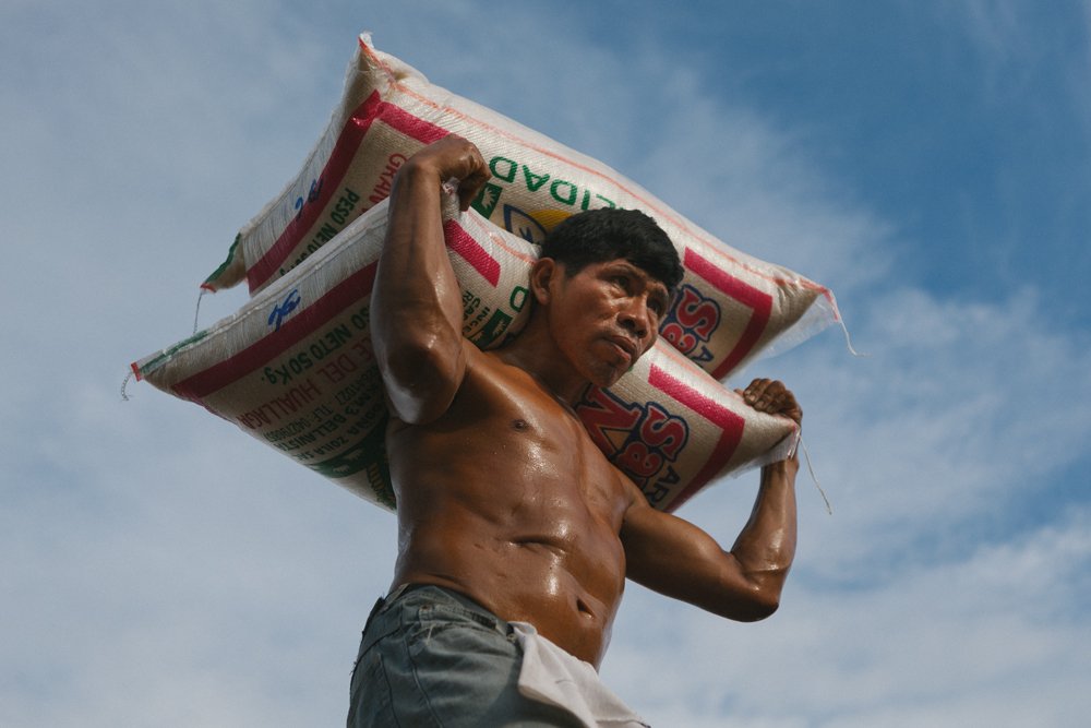 A laborer carries two 50-kilogram sacks of rice across his shoulders on a sunny day, Thursday, June 14, 2012, in Iquitos, Peru.