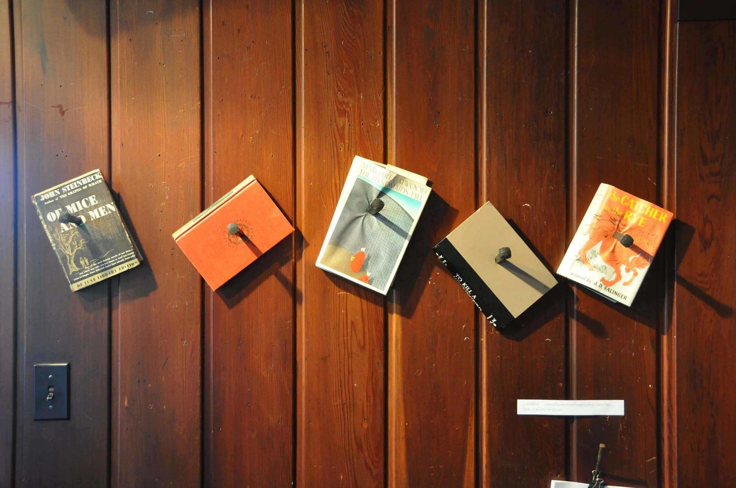 Display of several vintage books on a wooden shelf with a small informational plaque below.