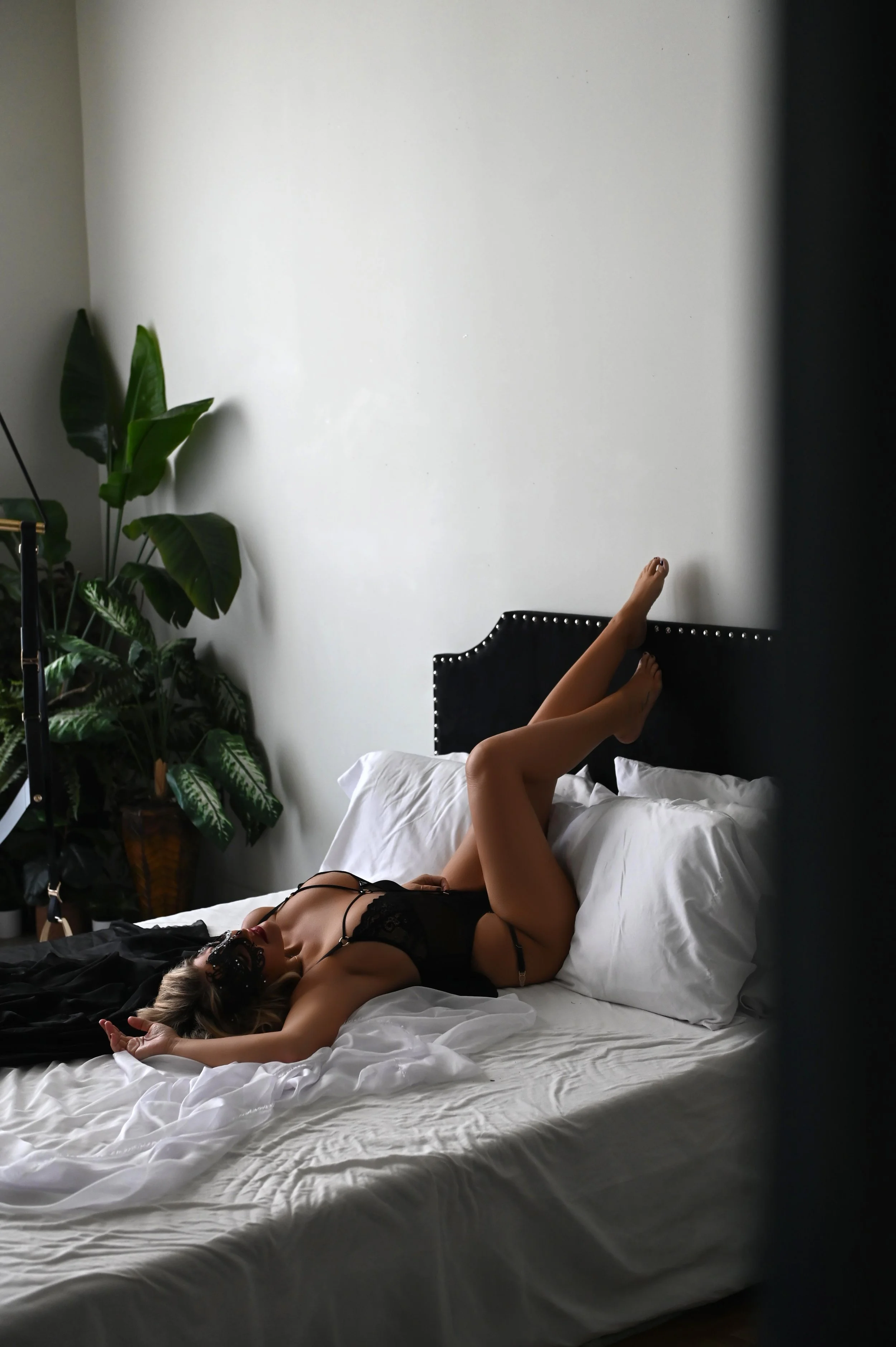 Dramatic wide-angle boudoir portrait on a white bed with soft natural window light