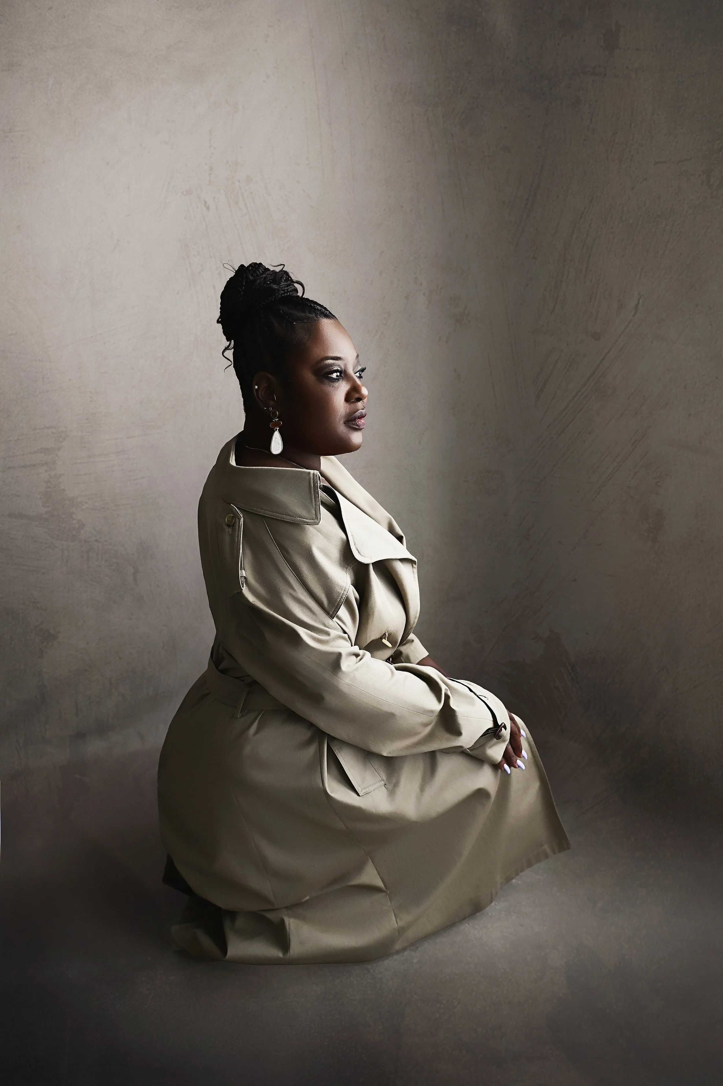 Dramatic seated boudoir portrait with neutral trench coat styling and moody lighting