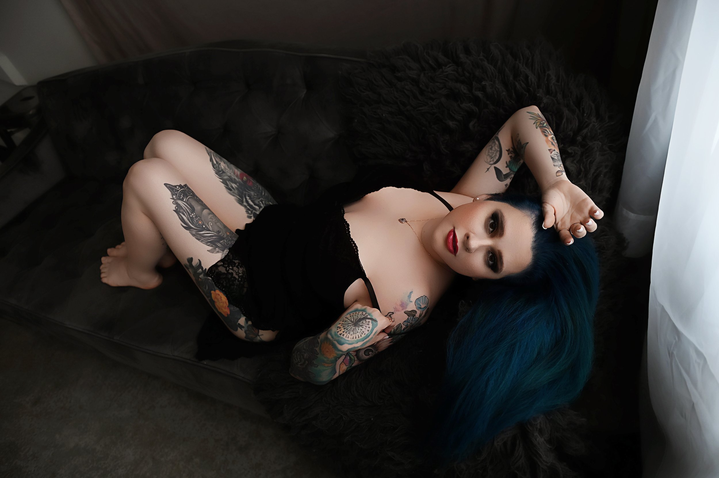 Woman in black lingerie reclining on a dark couch during a boudoir photography session