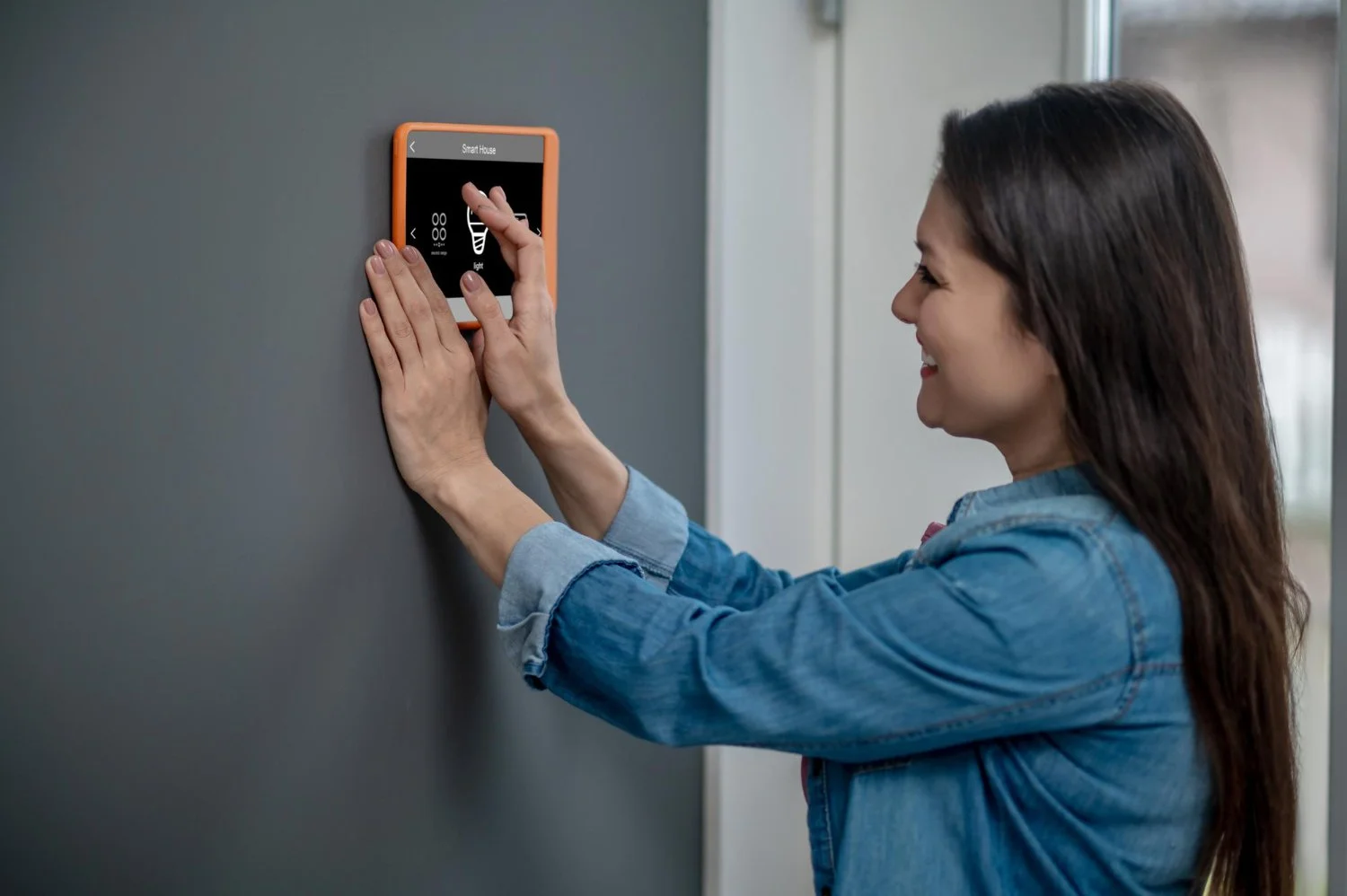 Woman in denim jacket touching a smart home control panel on a wall.