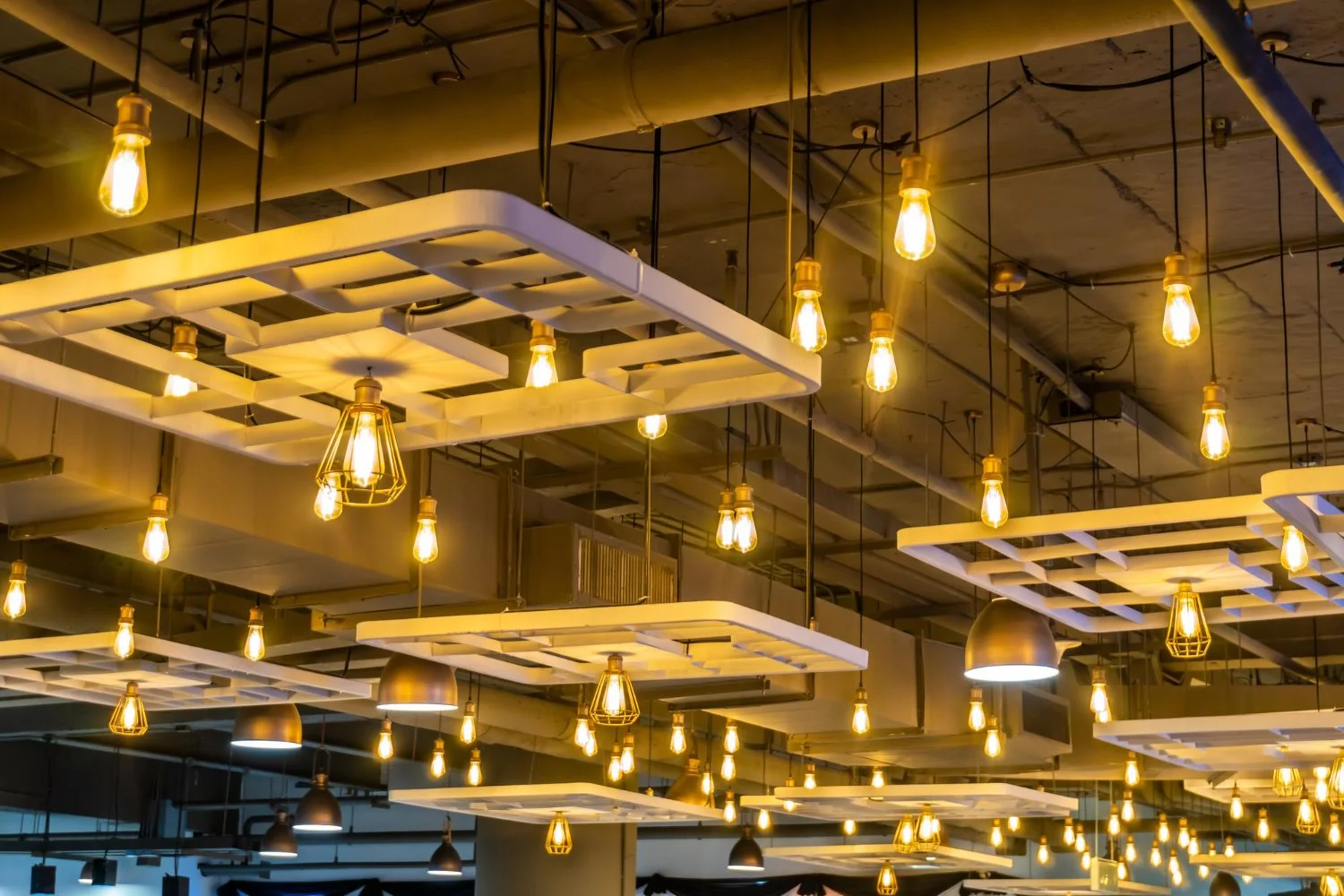 Ceiling with numerous hanging light bulbs and modern white light fixtures.