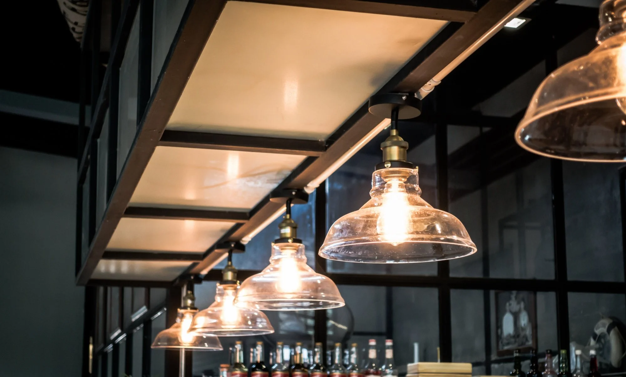 Ceiling lights with glass covers hanging above a bar counter area with bottles and a chalkboard menu.