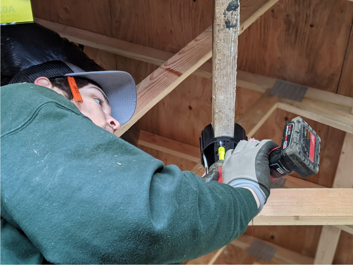 A man using a cordless power drill to drill into a wooden stud in a building under construction.